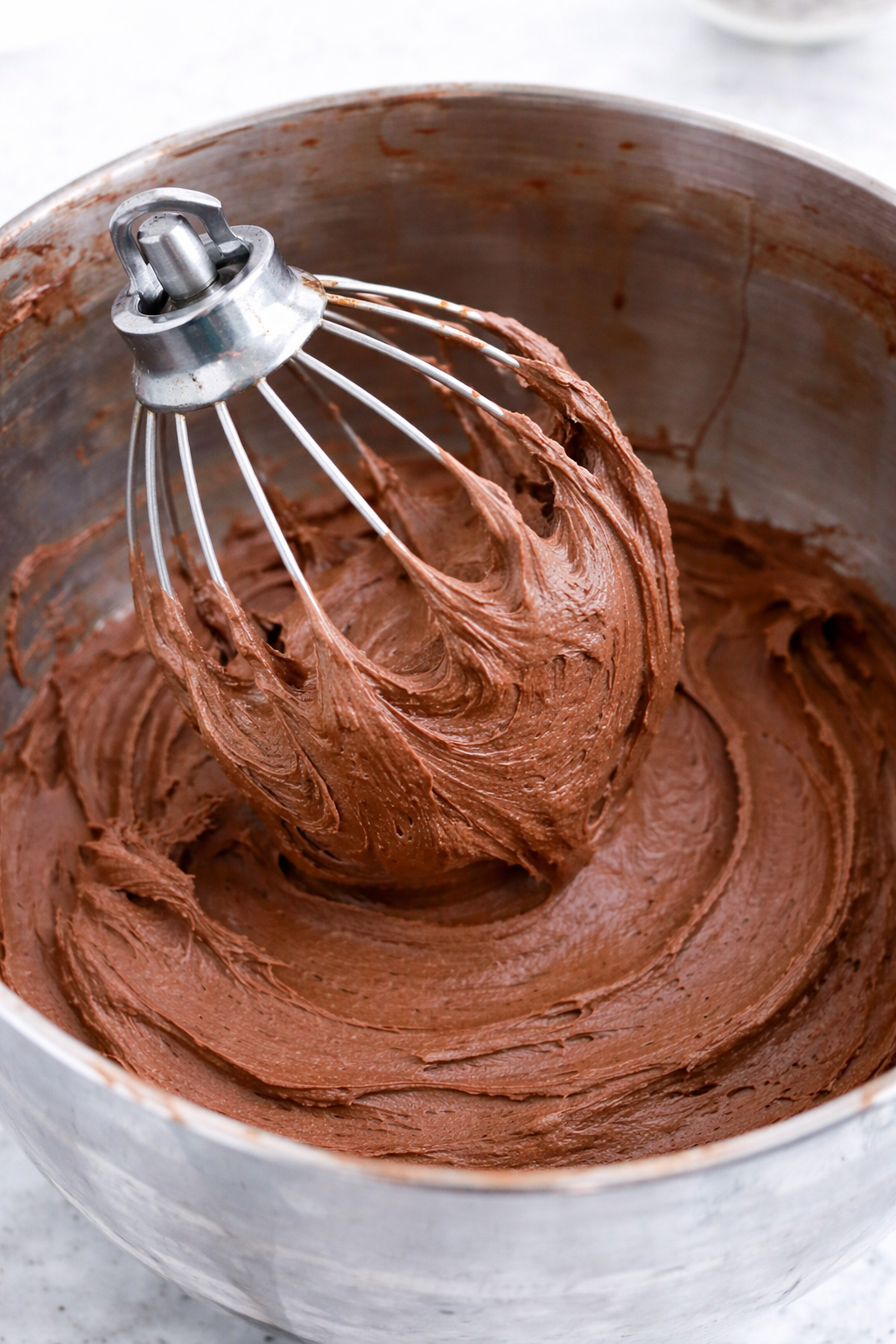 Chocolate Buttercream Frosting in a mixing bowl with a whisk lifting some up