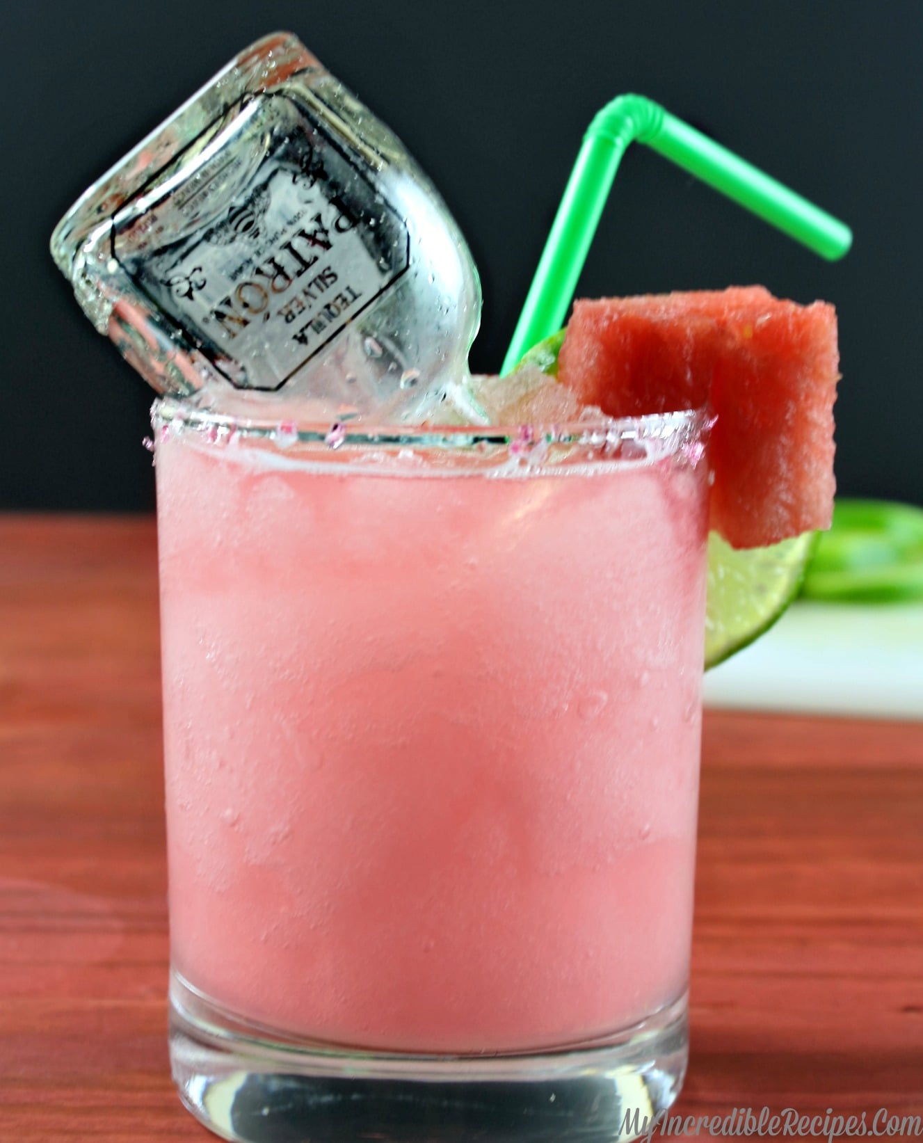 close up of watermelon margarita on a wood table with a mini bottle of patron inside