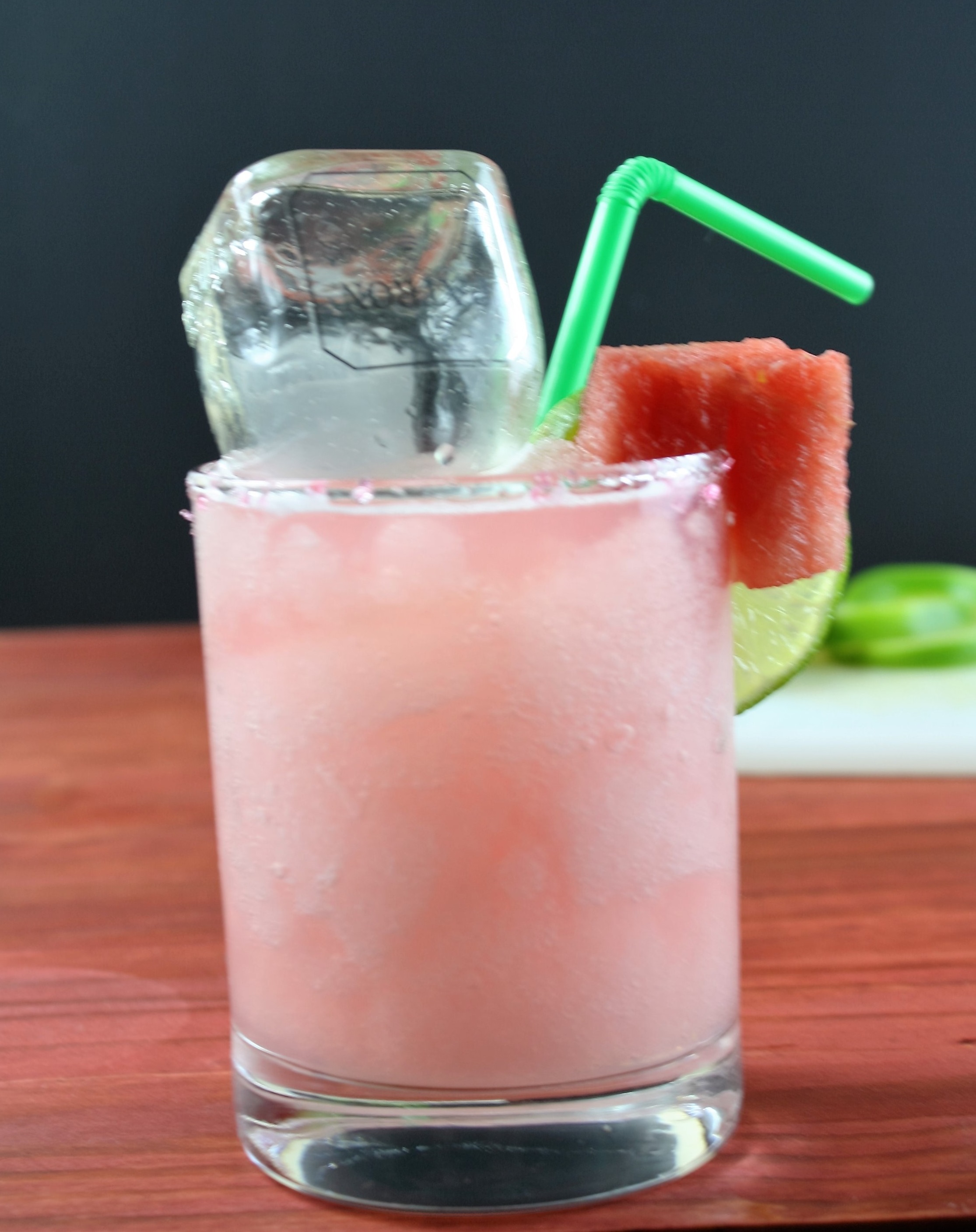 watermelon margarita on a wood table with a mini bottle of patron inside