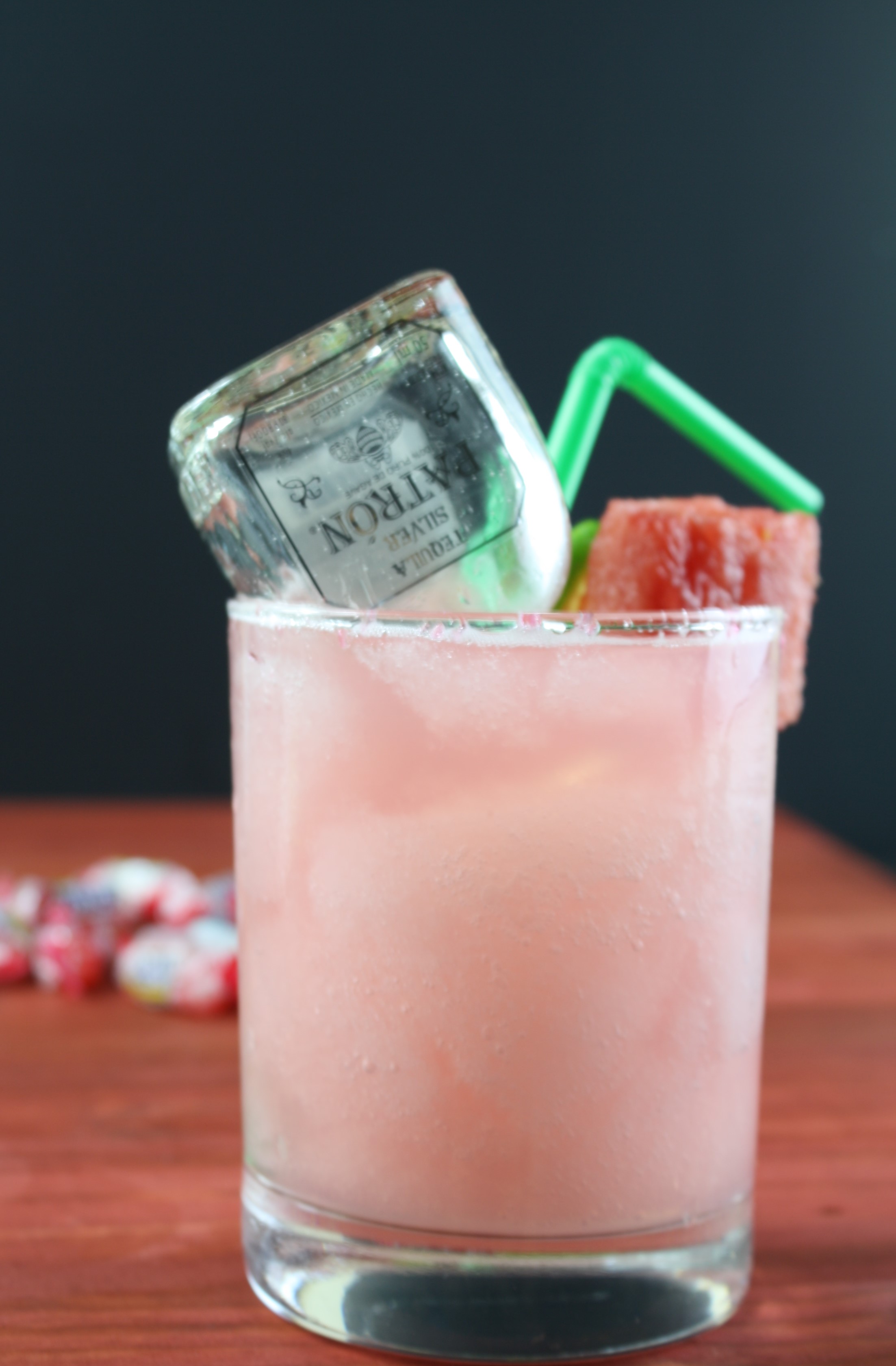 watermelon margarita on a wood table with a mini bottle of patron inside