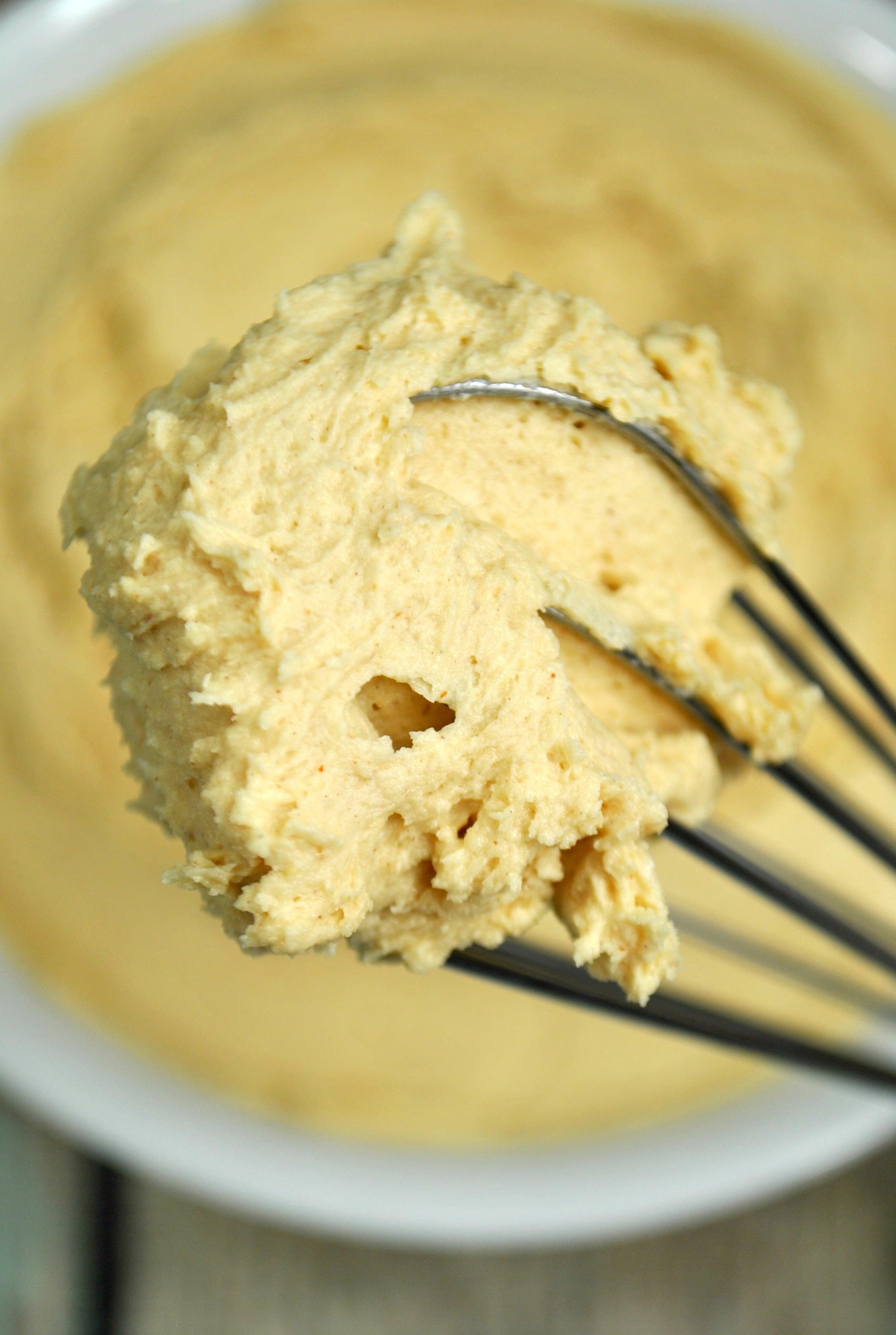 Peanut Butter Frosting in a metal mixing bowl being lifted by a whisk