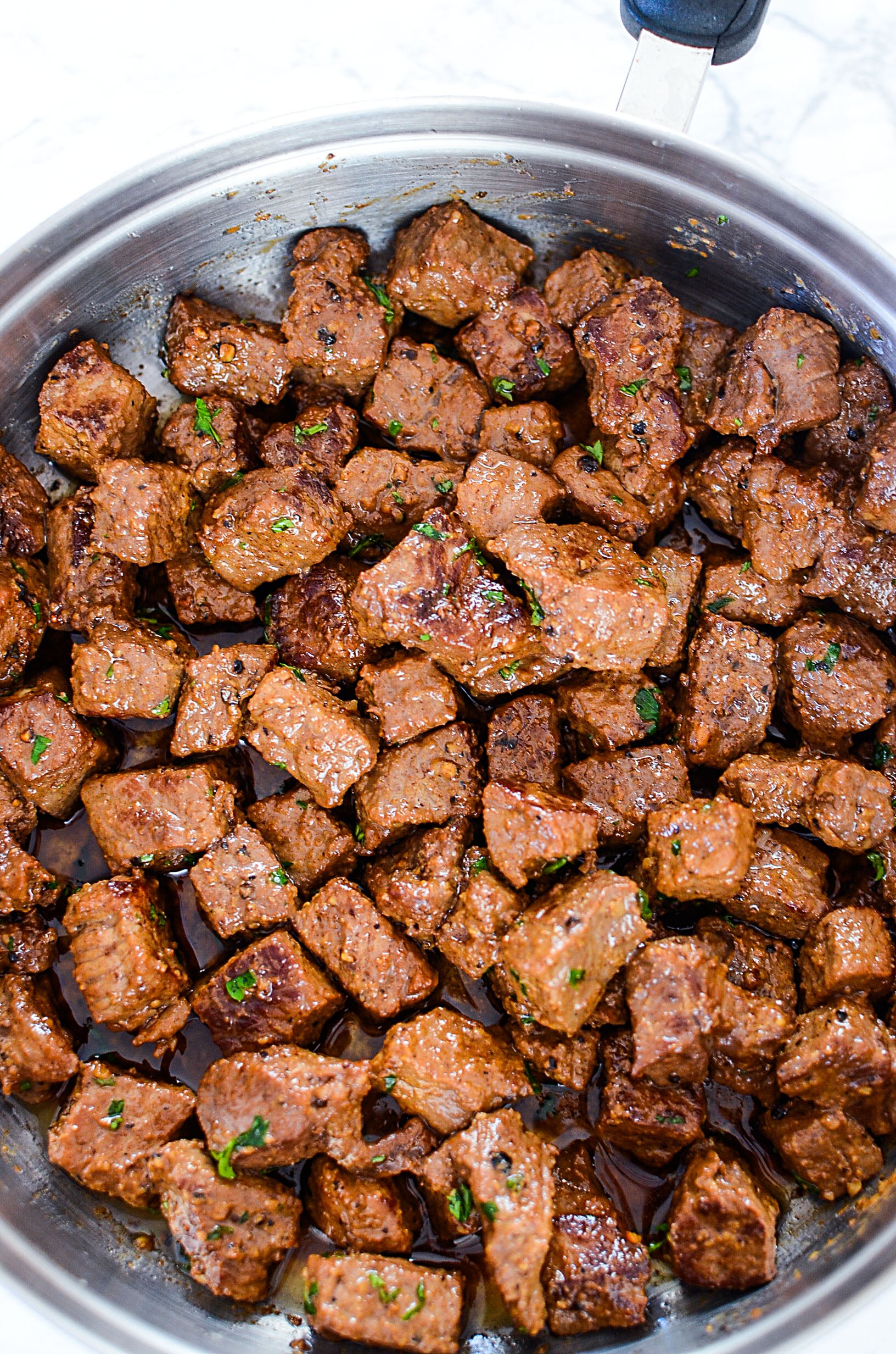 overhead shot of Juicy Garlic Butter Steak Bites in a skillet covered in garlic butter