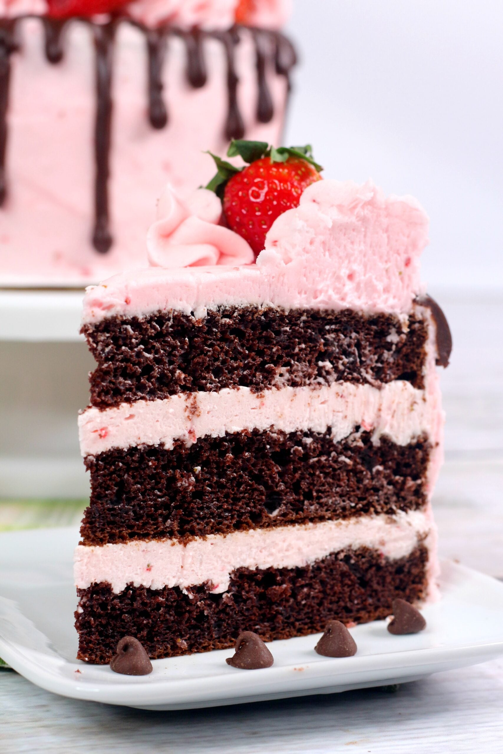 Chocolate Kahlua Cake Slice with Strawberry Buttercream Frosting on a white plate with the whole cake in the background