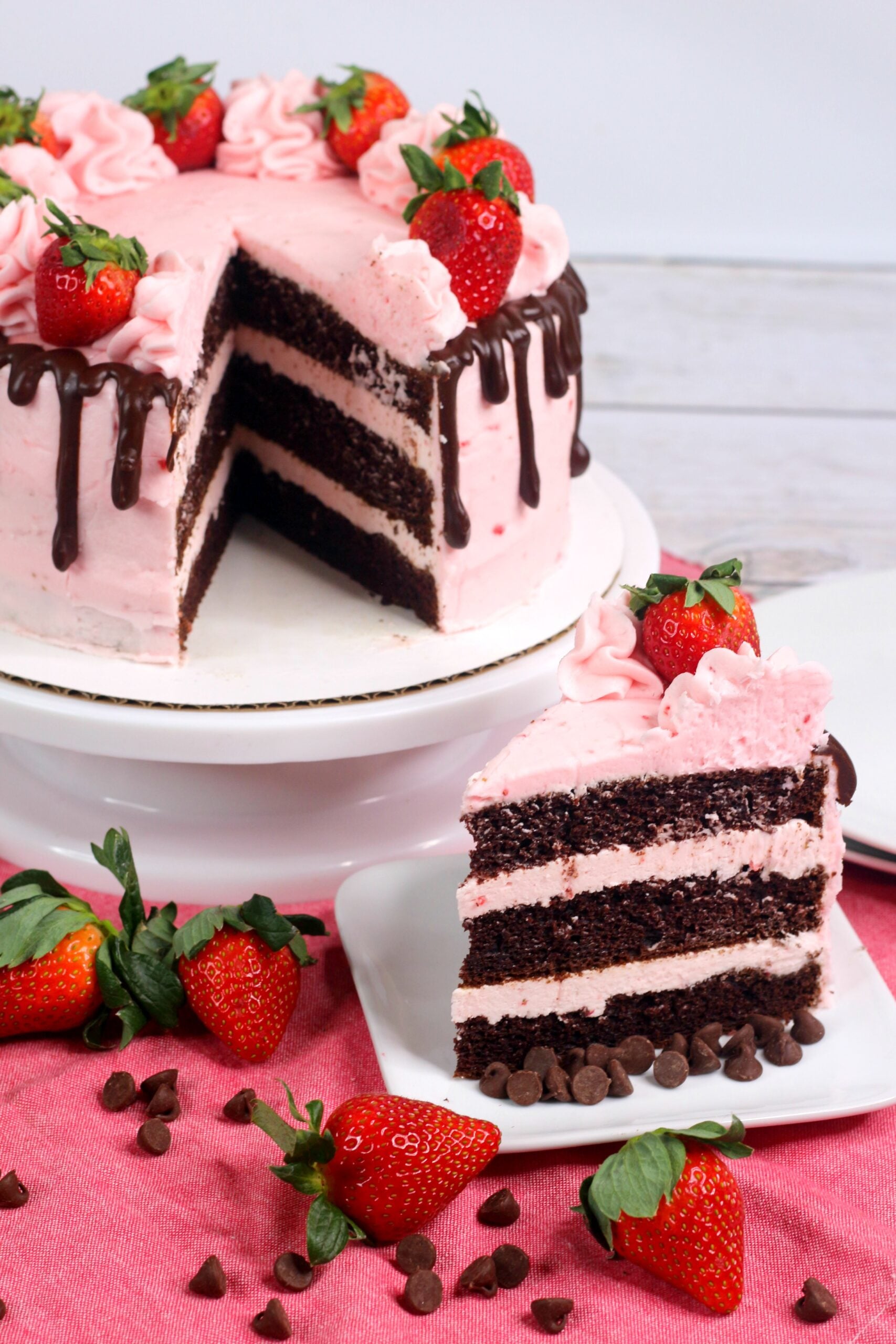 Overhead side view of the Chocolate Kahlua Cake Slice with Strawberry Buttercream Frosting on a white plate with the whole cake in the background