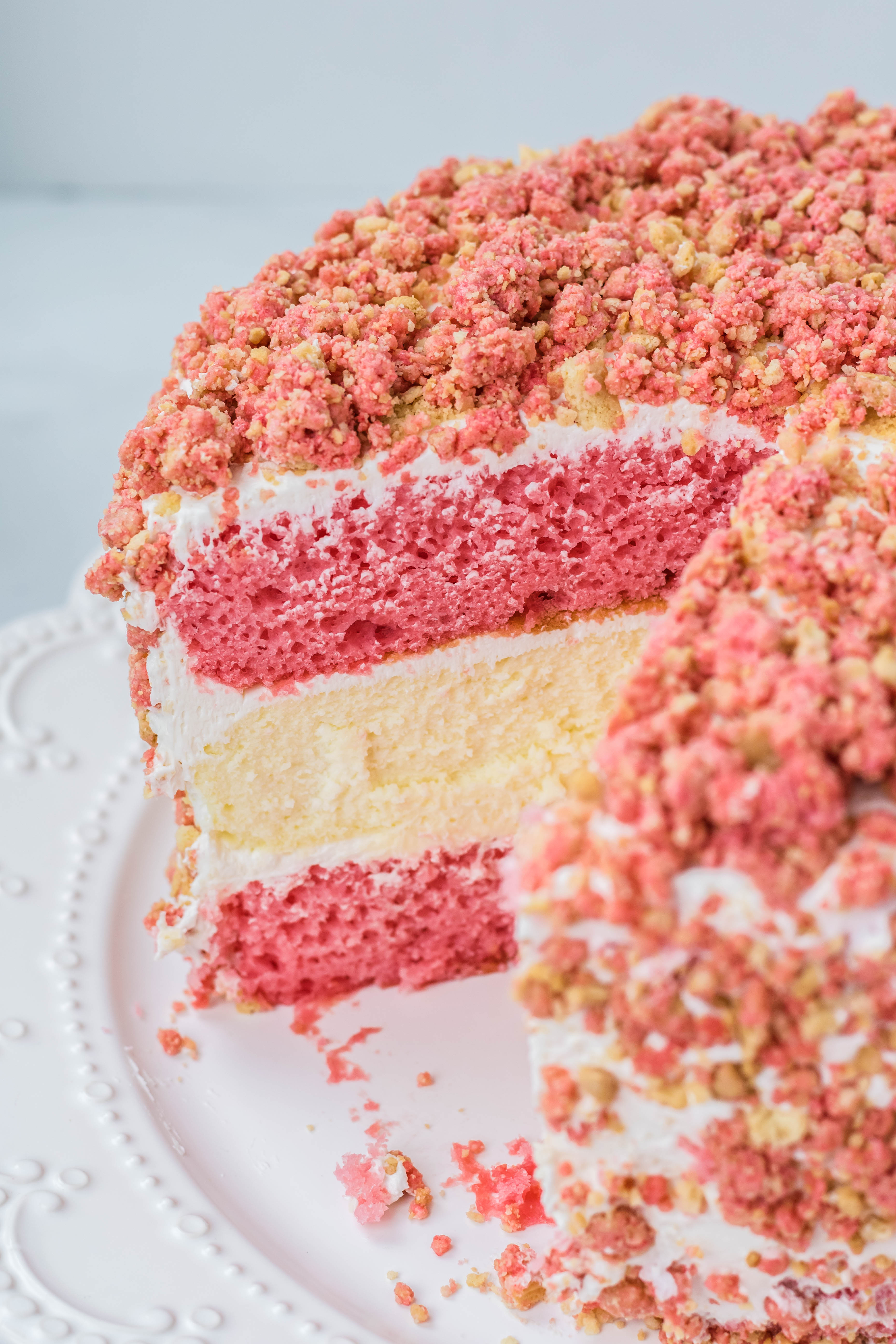 Strawberry Shortcake Cheesecake Cake on a white serving cake dish with a slice missing
