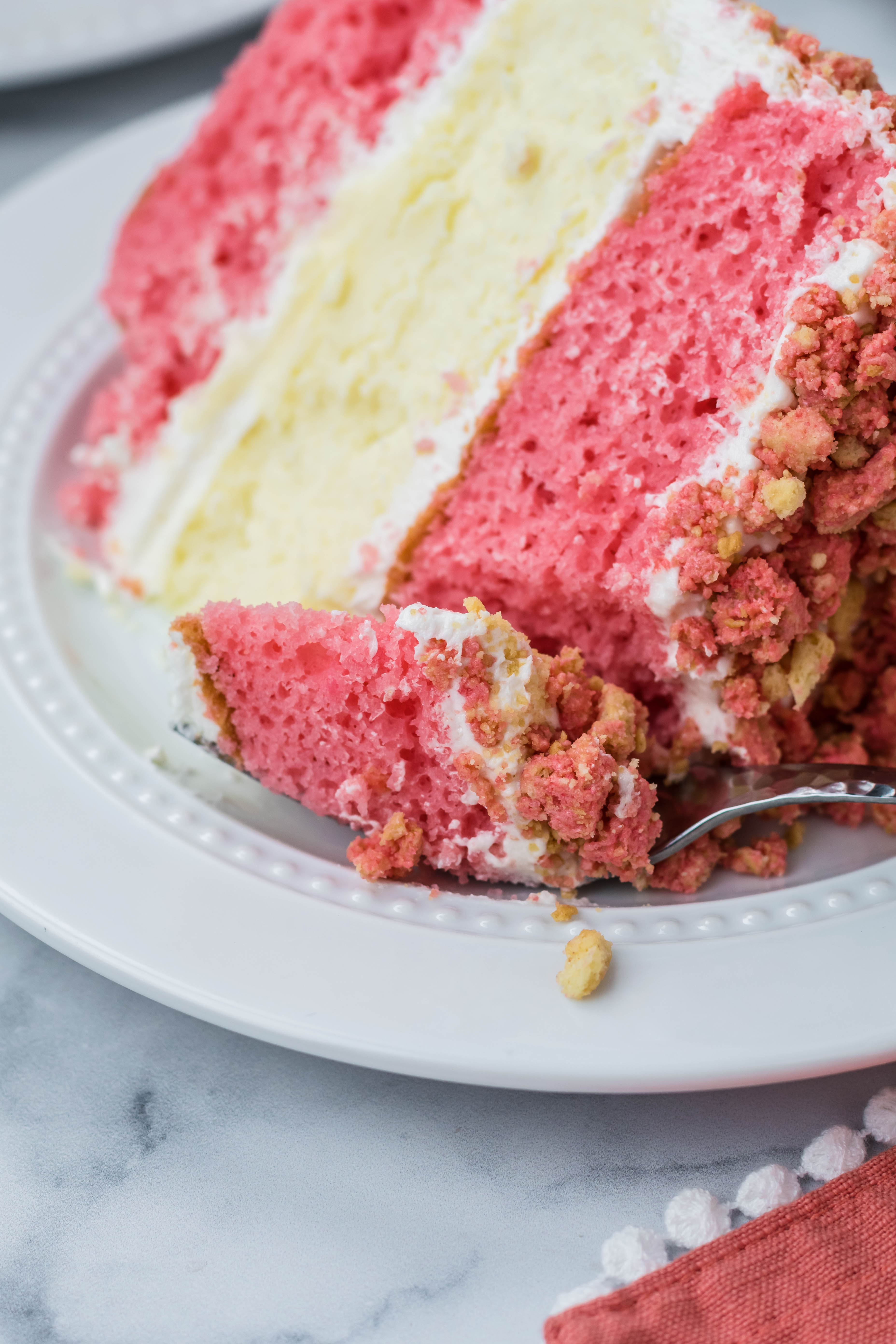 Up close shot of the Strawberry Shortcake Cheesecake Cake slice on a white plate with a fork taking a bite out