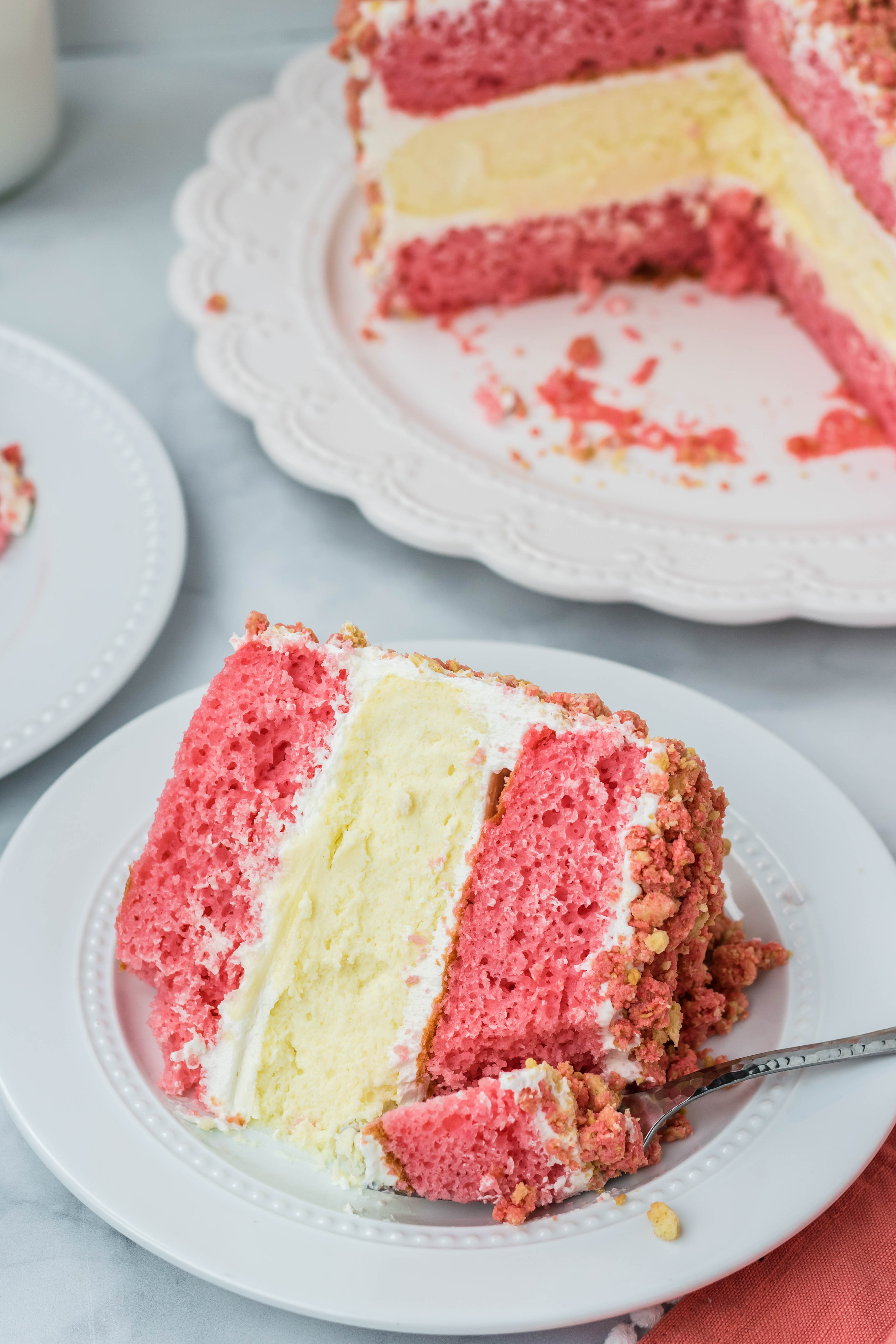 overhead shot of the Strawberry Shortcake Cheesecake Cake on a white plate with a fork taking a bite out