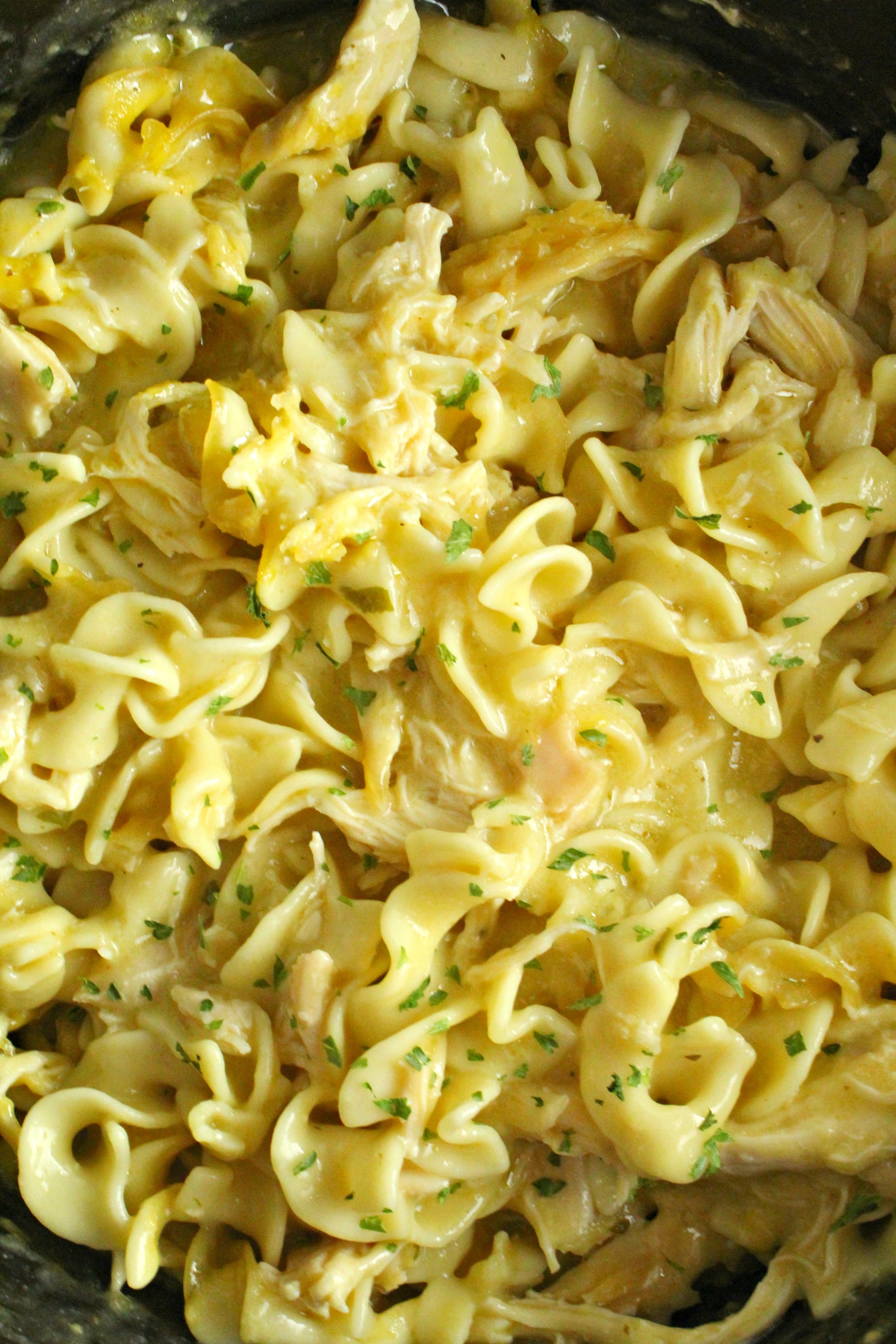 Slow Cooker Chicken and Noodles up close in a slow cooker with a spoon lifting up a bite 