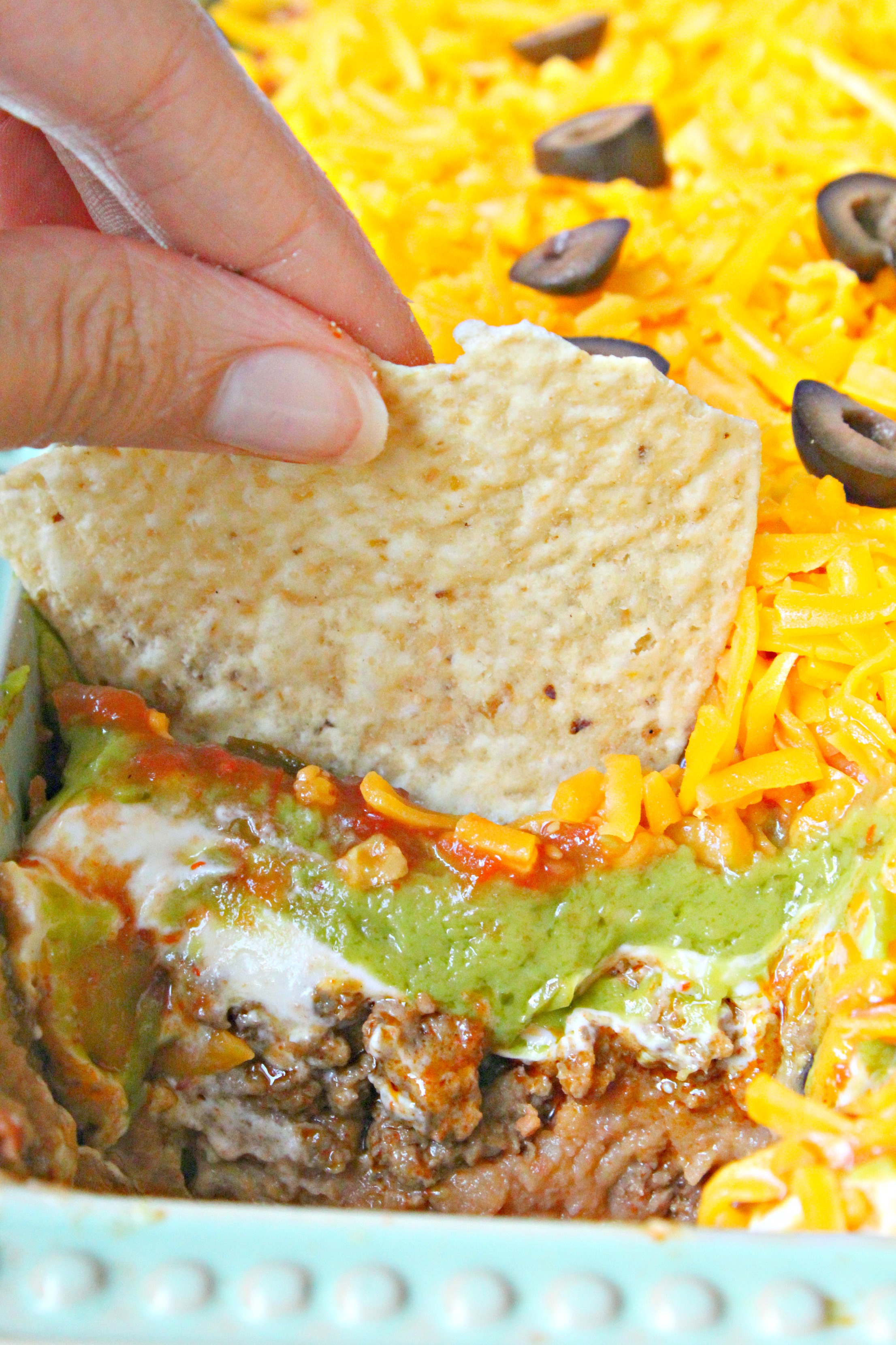 7 layer taco dip with a tortilla chip being dipped in