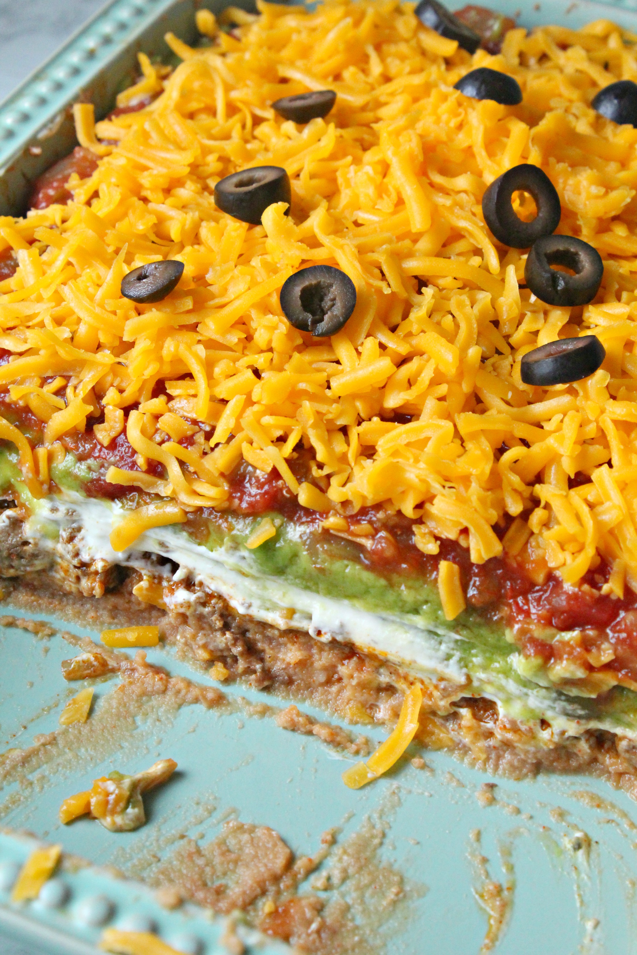 7 layer taco dip with half missing in a blue baking dish