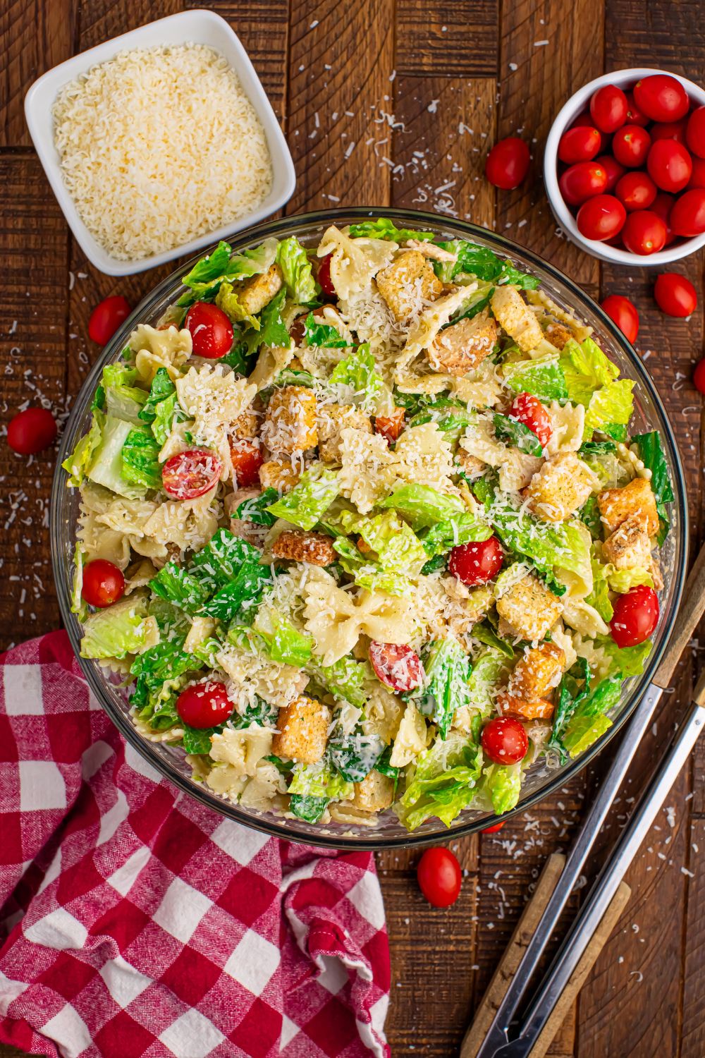 Chicken Caesar Pasta Salad in a bowl on table with a bowl of tomatos and abowl of parmesan cheese in little bowls beside it 