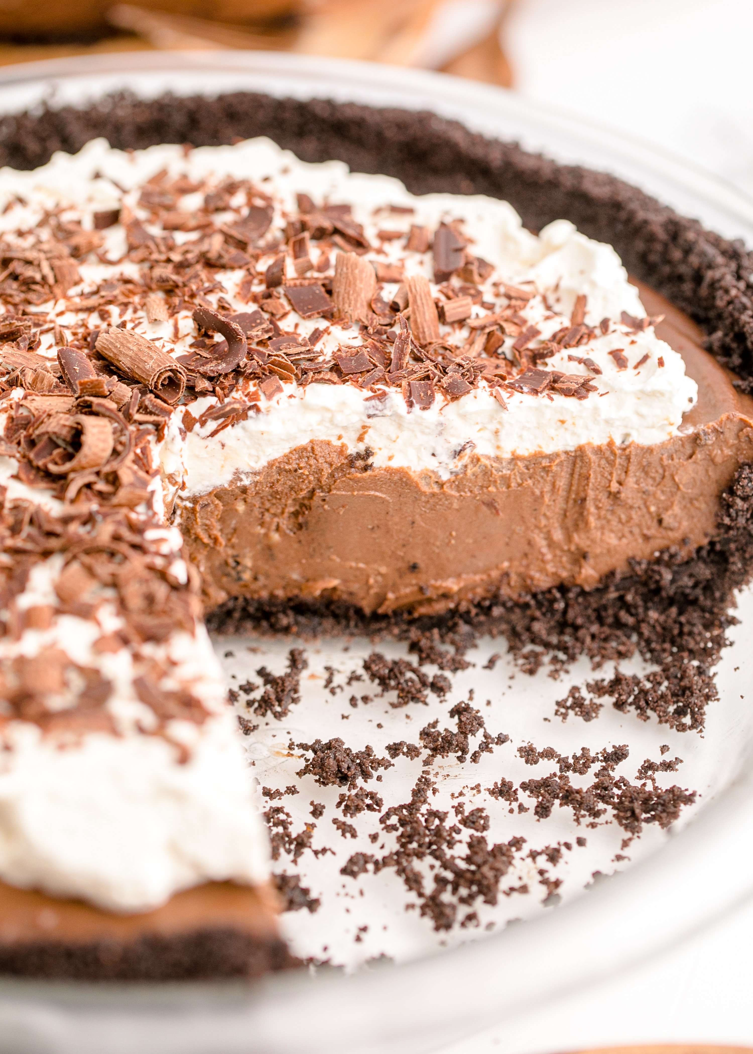 Chocolate Cream Pie topped with whipped cream and chocolate shavings on a white pie dish with a slice cut out