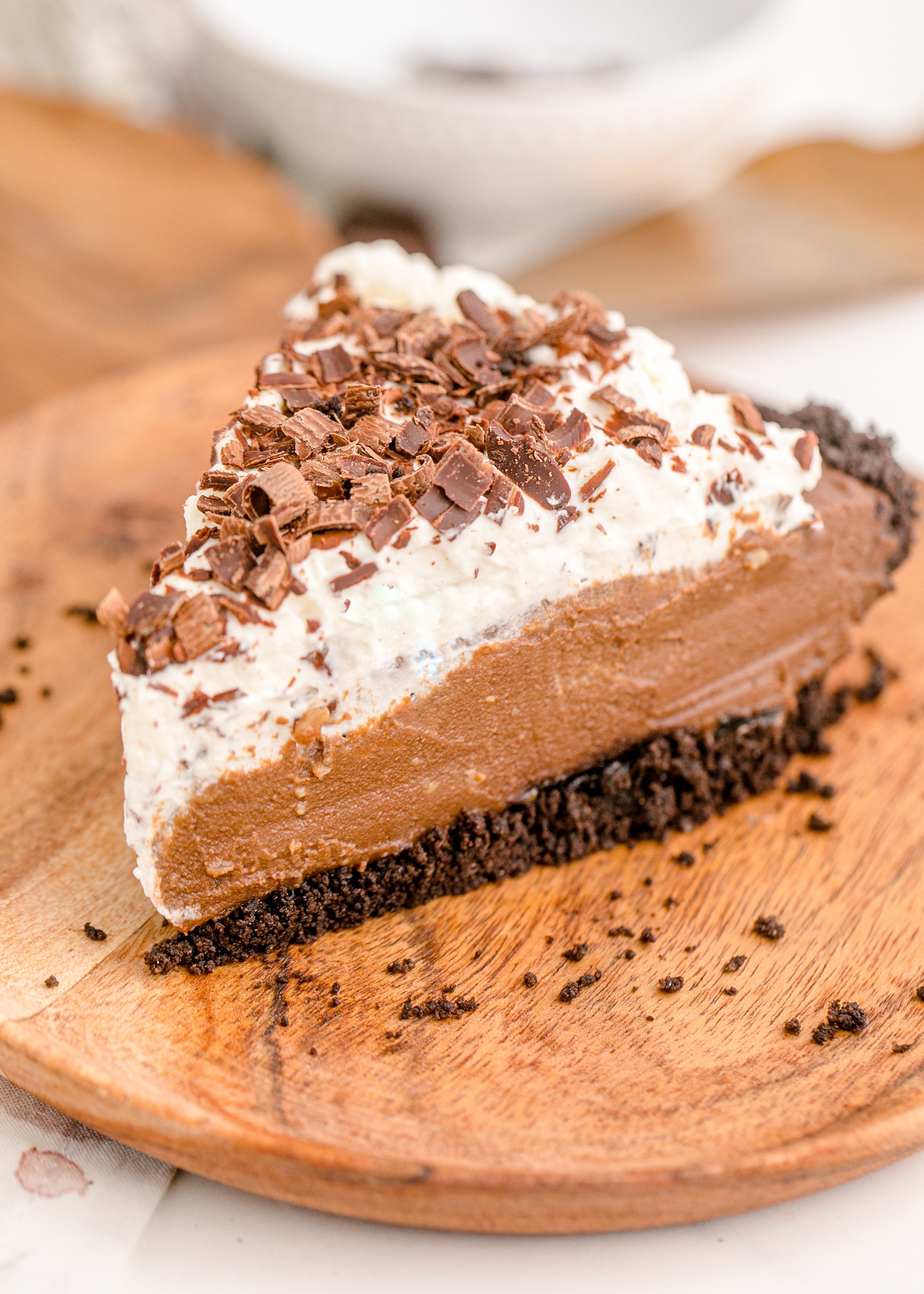 Chocolate Cream Pie topped with whipped cream and chocolate shavings on a a brown cutting board