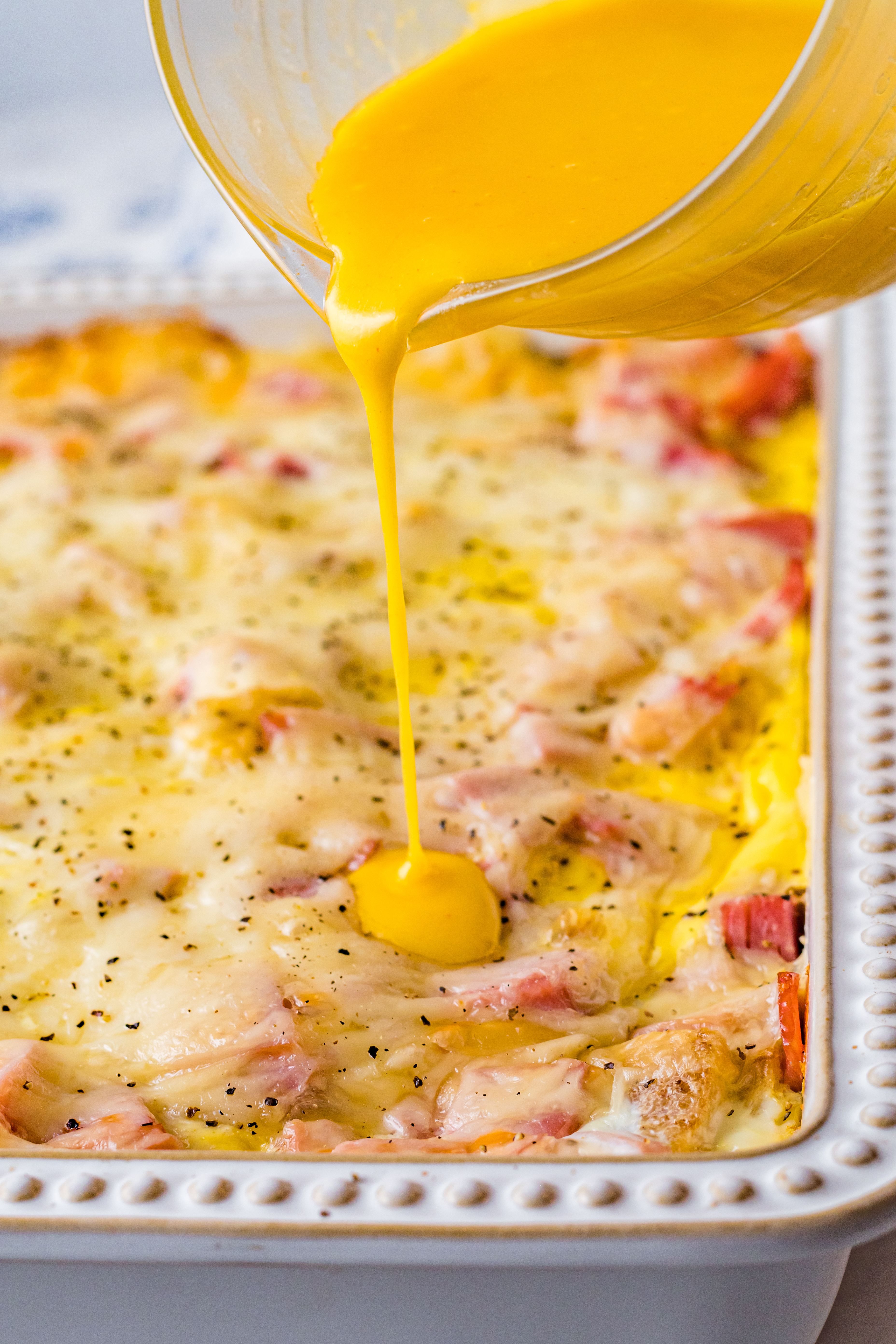 Eggs Benedict in a white casserole dish with hollandaise sauce being poured on top