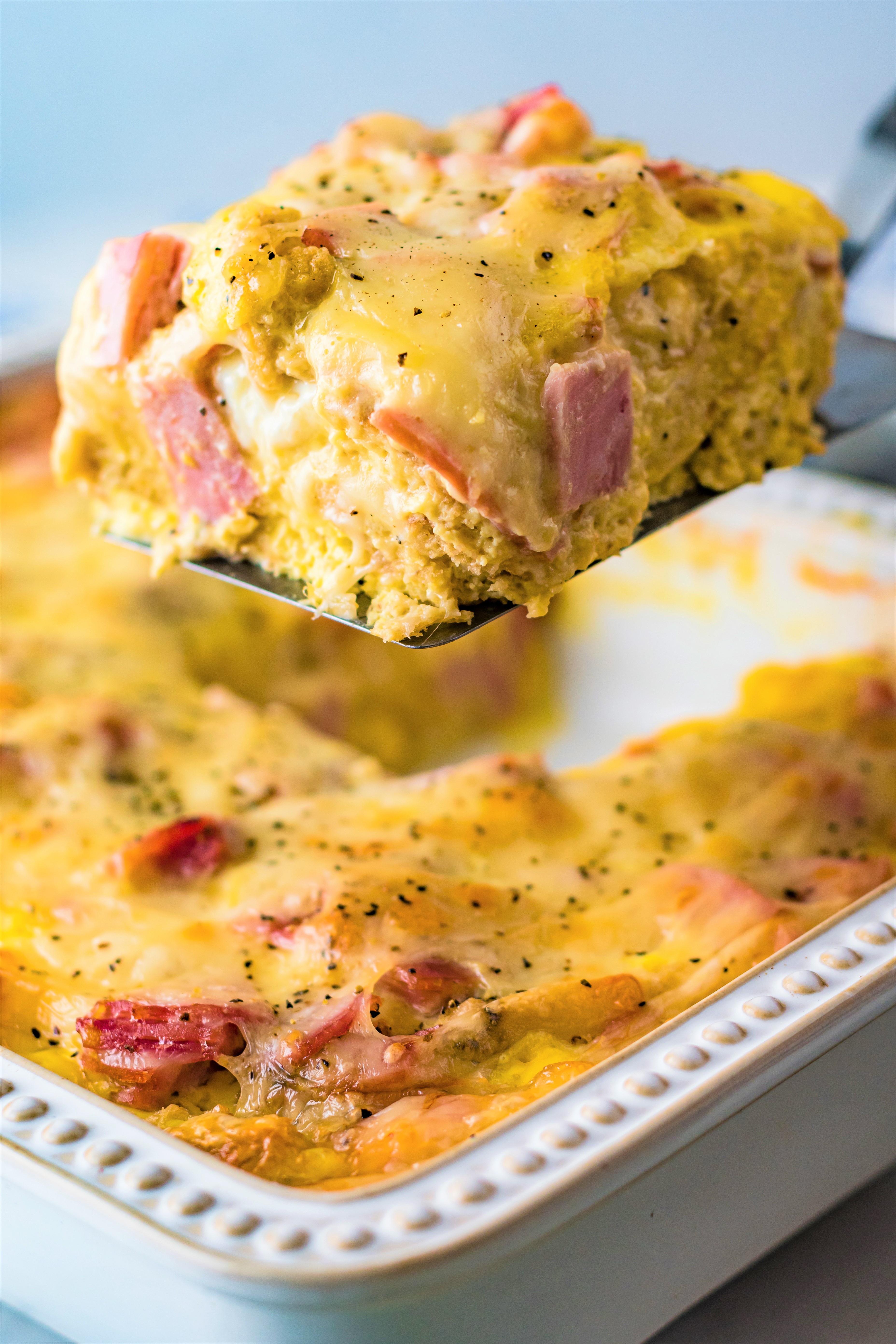 Eggs Benedict in a white casserole dish with a slice being lifted out on a spatula