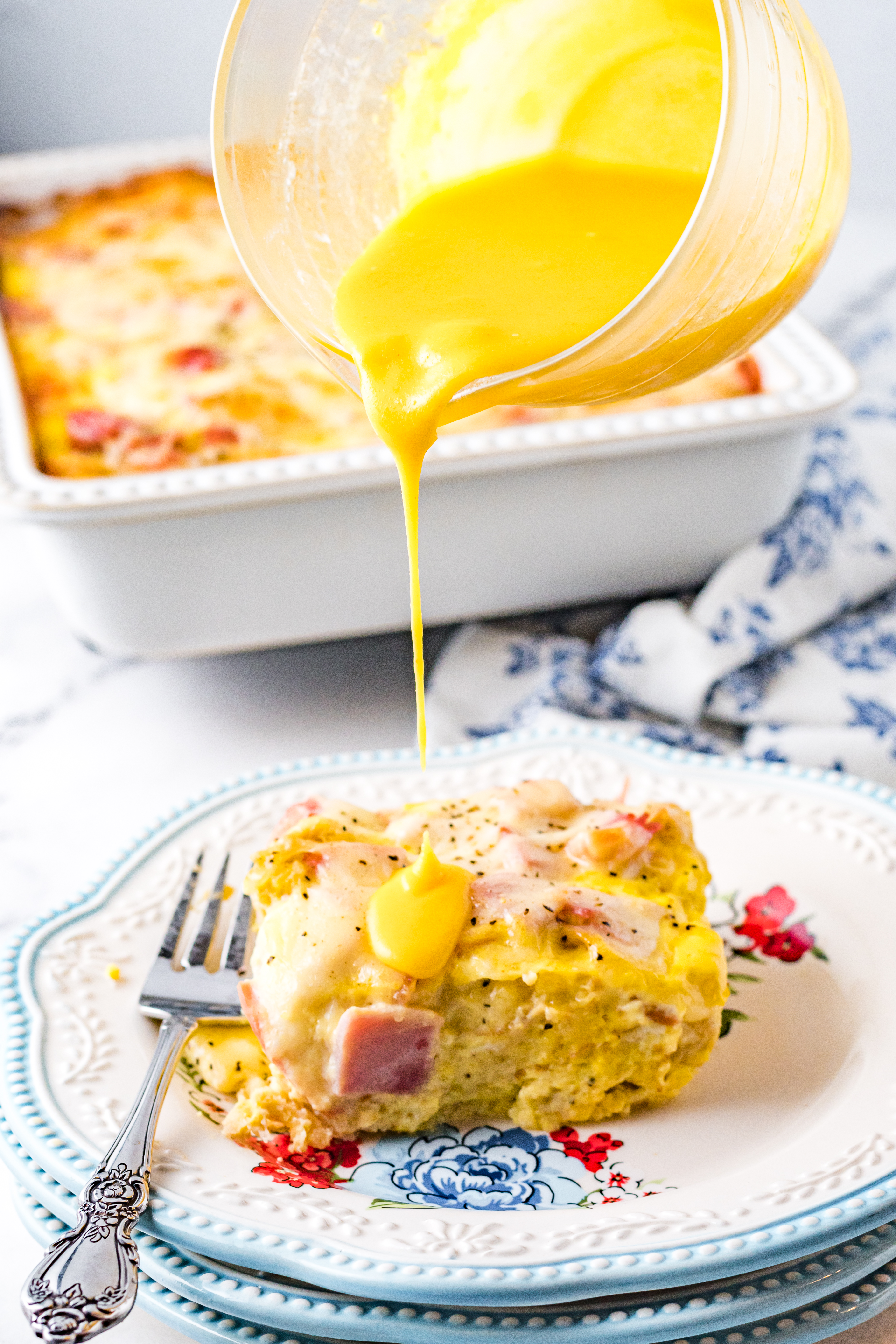 Eggs Benedict slice on a white plate with the hollandaise sauce being poured on top of the slice