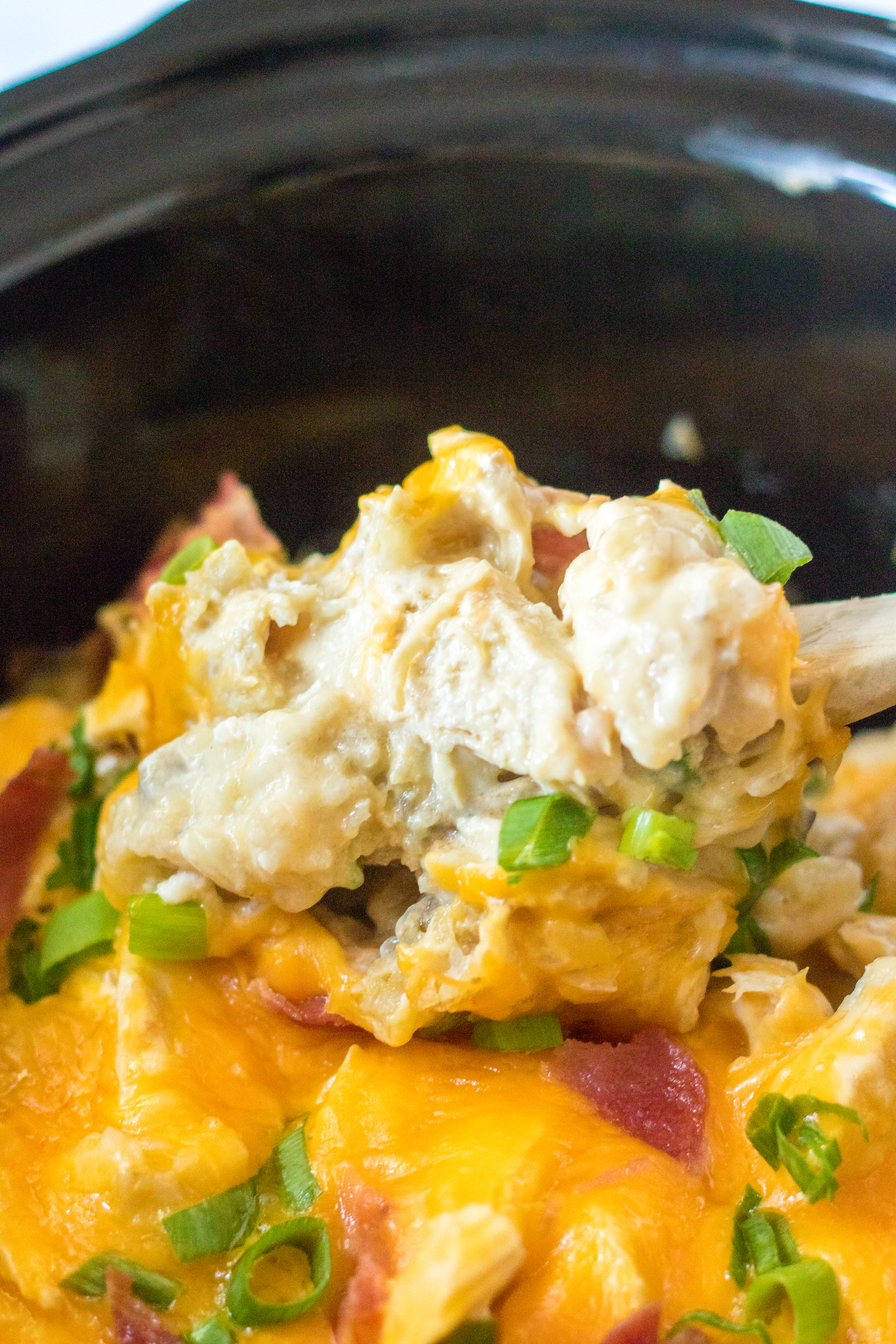 slow cooker photo of a spoon lifting the chicken covered in cheese and tater tots