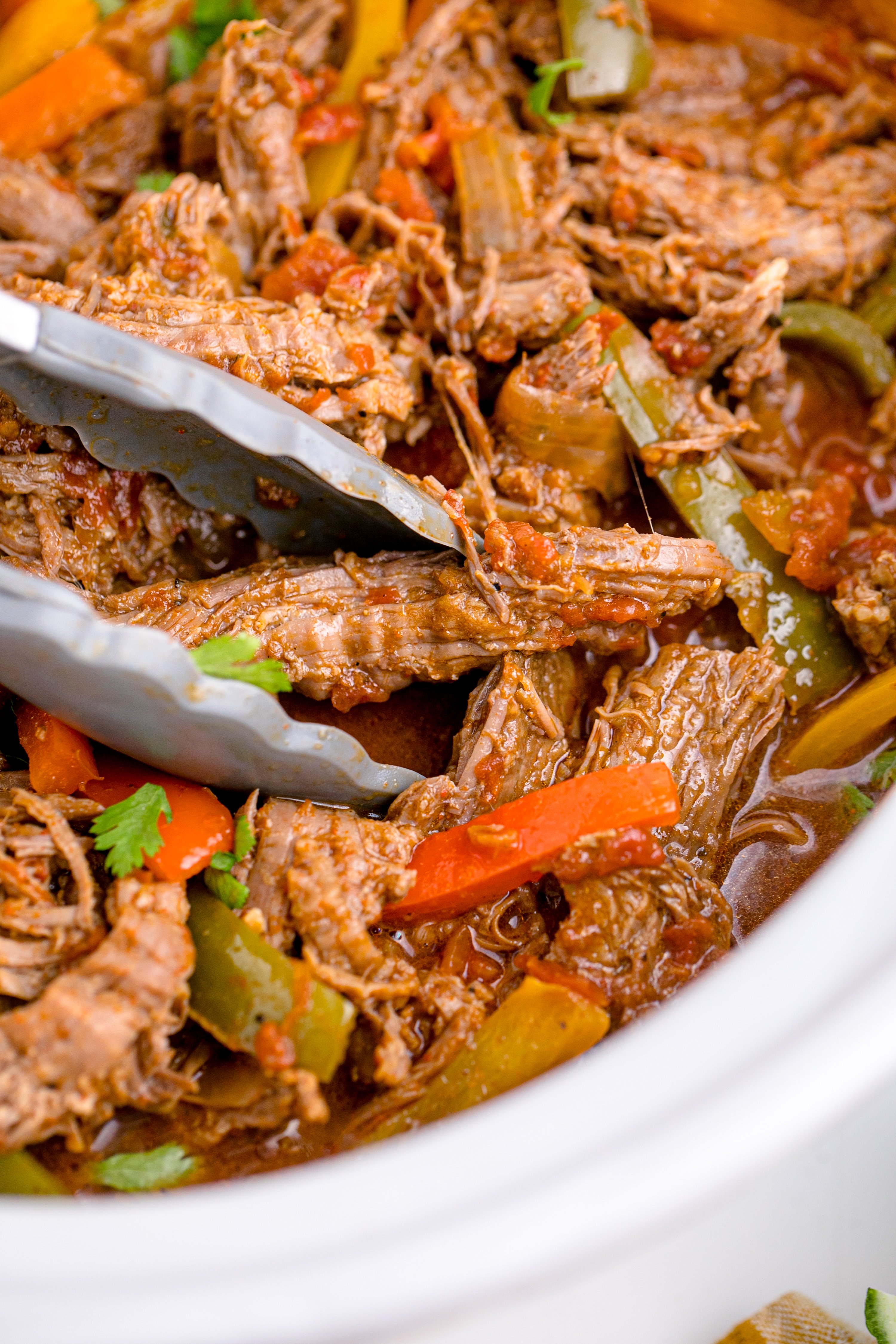 Steak Fajitas in a white crock pot being lifted with tongs