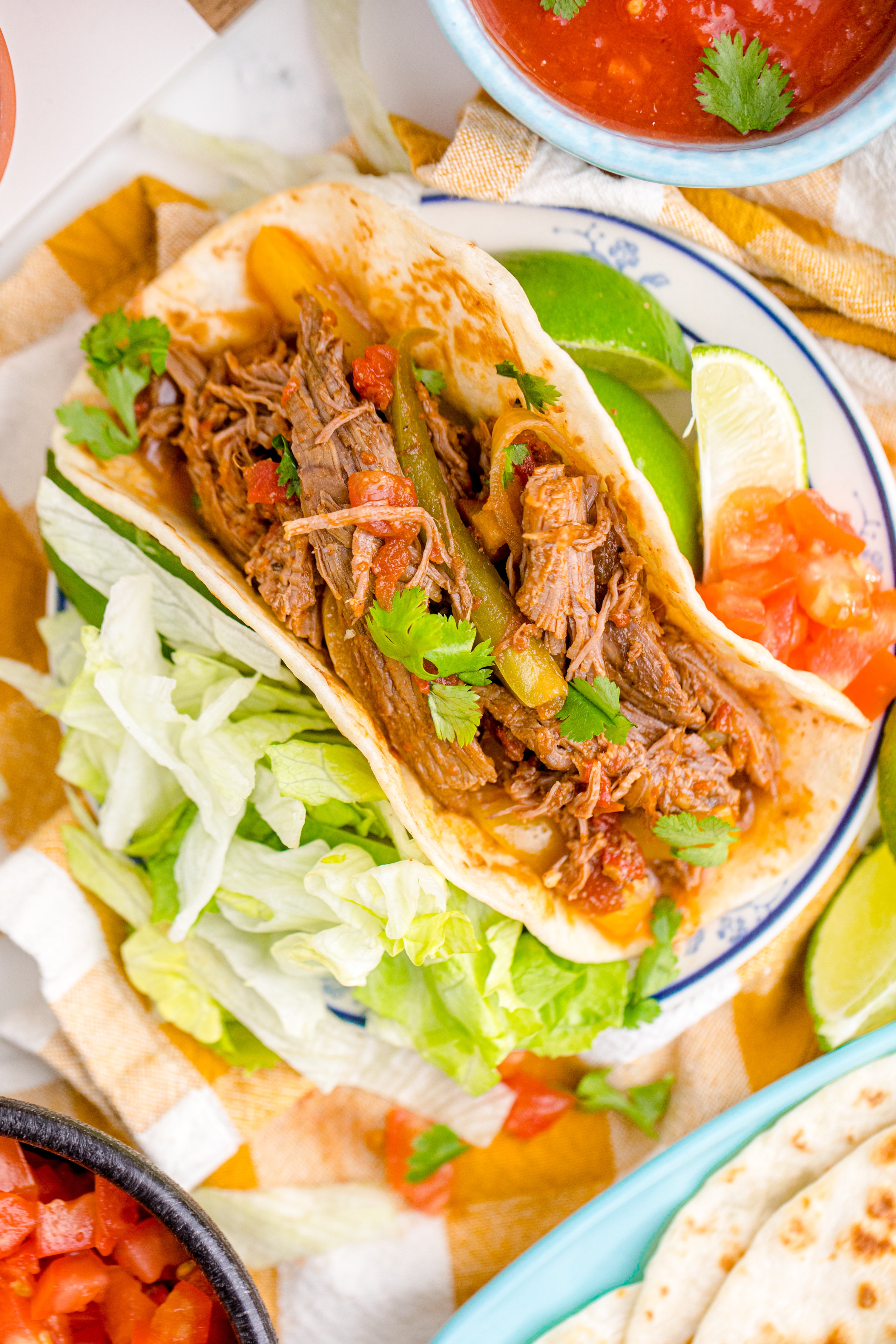 Steak Fajitas wrapped in a tortilla with lettuce piled next to it and limes with salsa