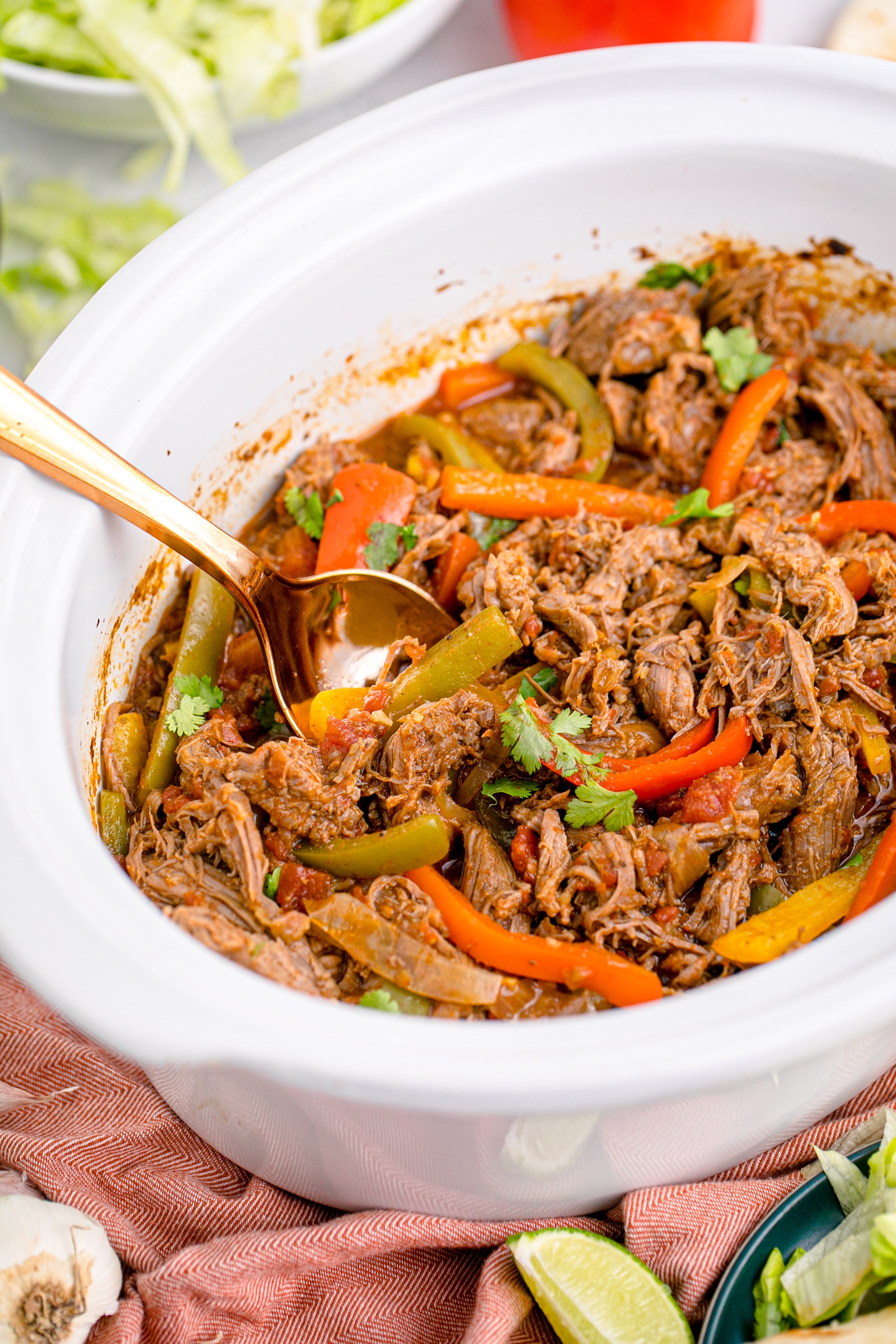 Steak Fajitas in a white crock pot with a gold spoon