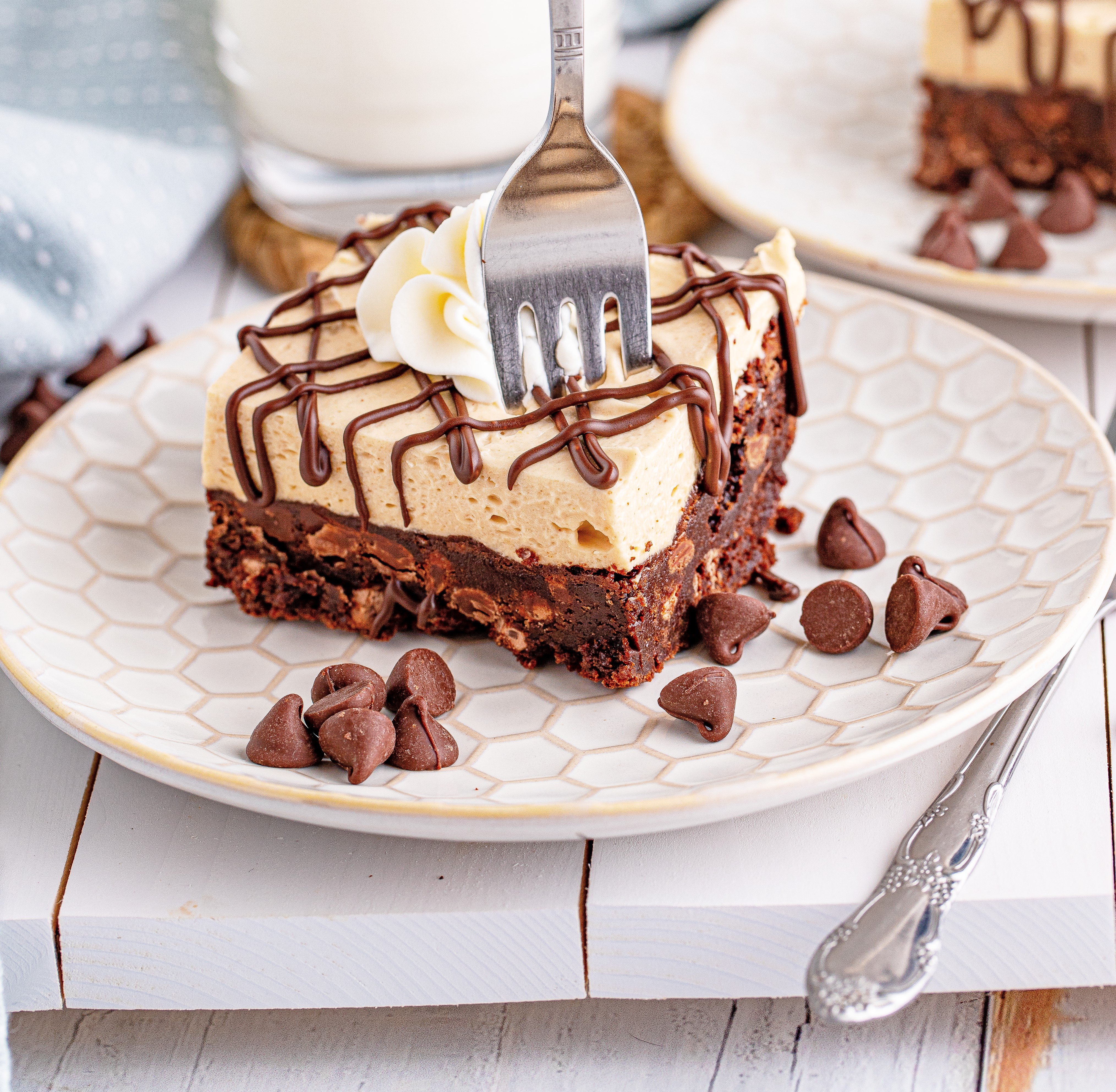 Peanut Butter Brownies on a white place drizzeled with chocolate and topped with whipped cream with a forn going through the brownie