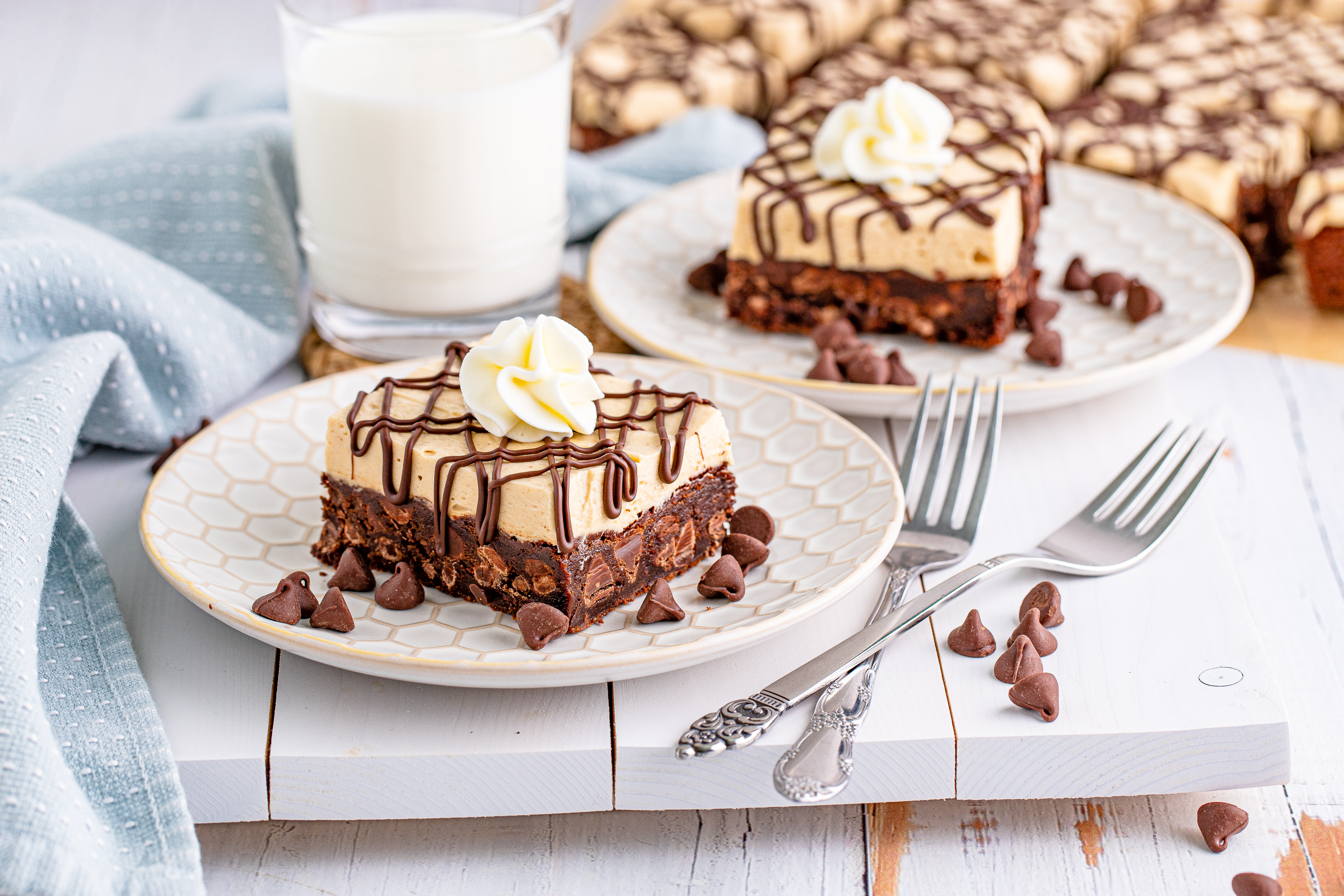 Peanut Butter Brownies on a white place drizzeled with chocolate and topped with whipped cream and a cup of milk