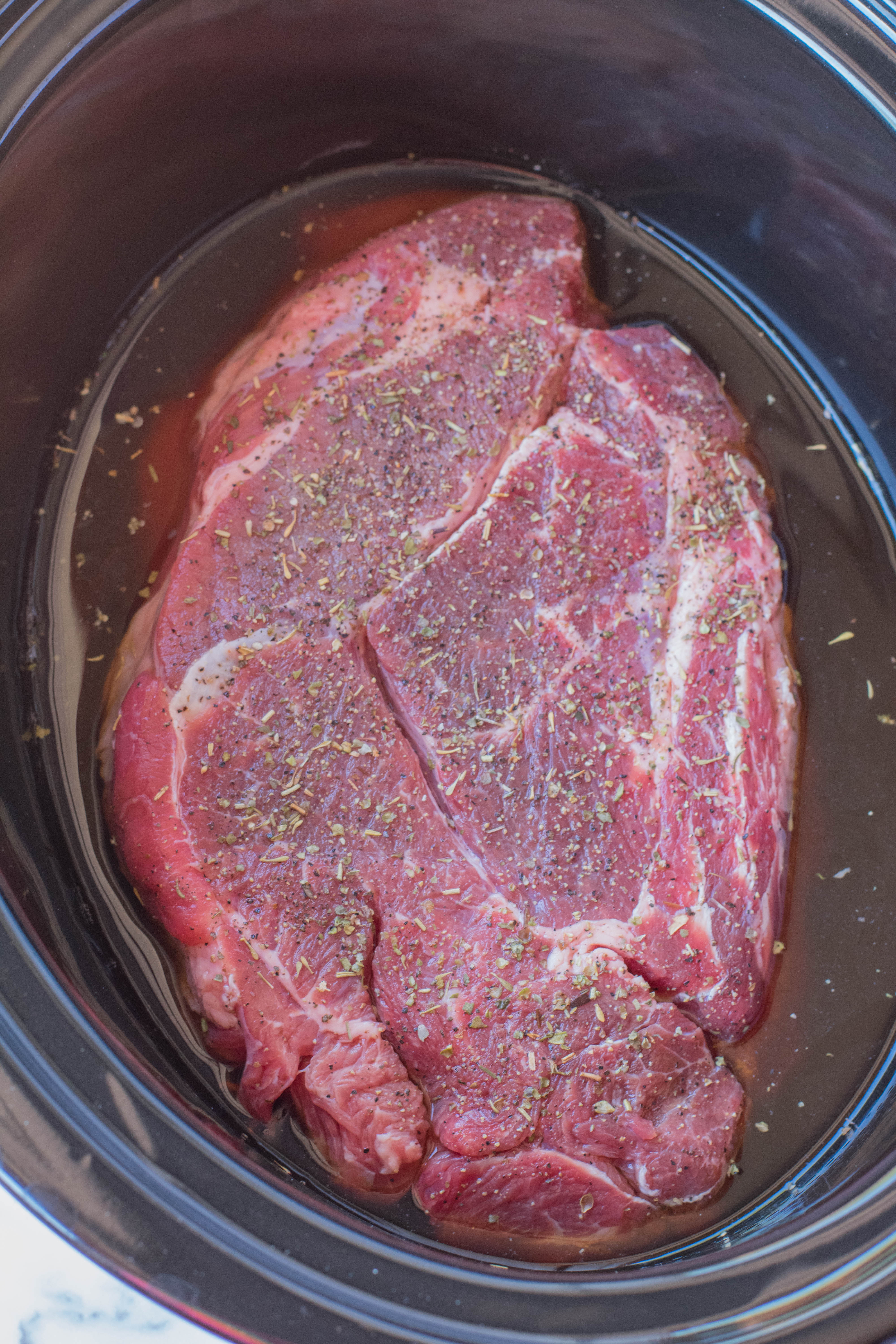 crock pot chuck roast in a black crock pot uncooked