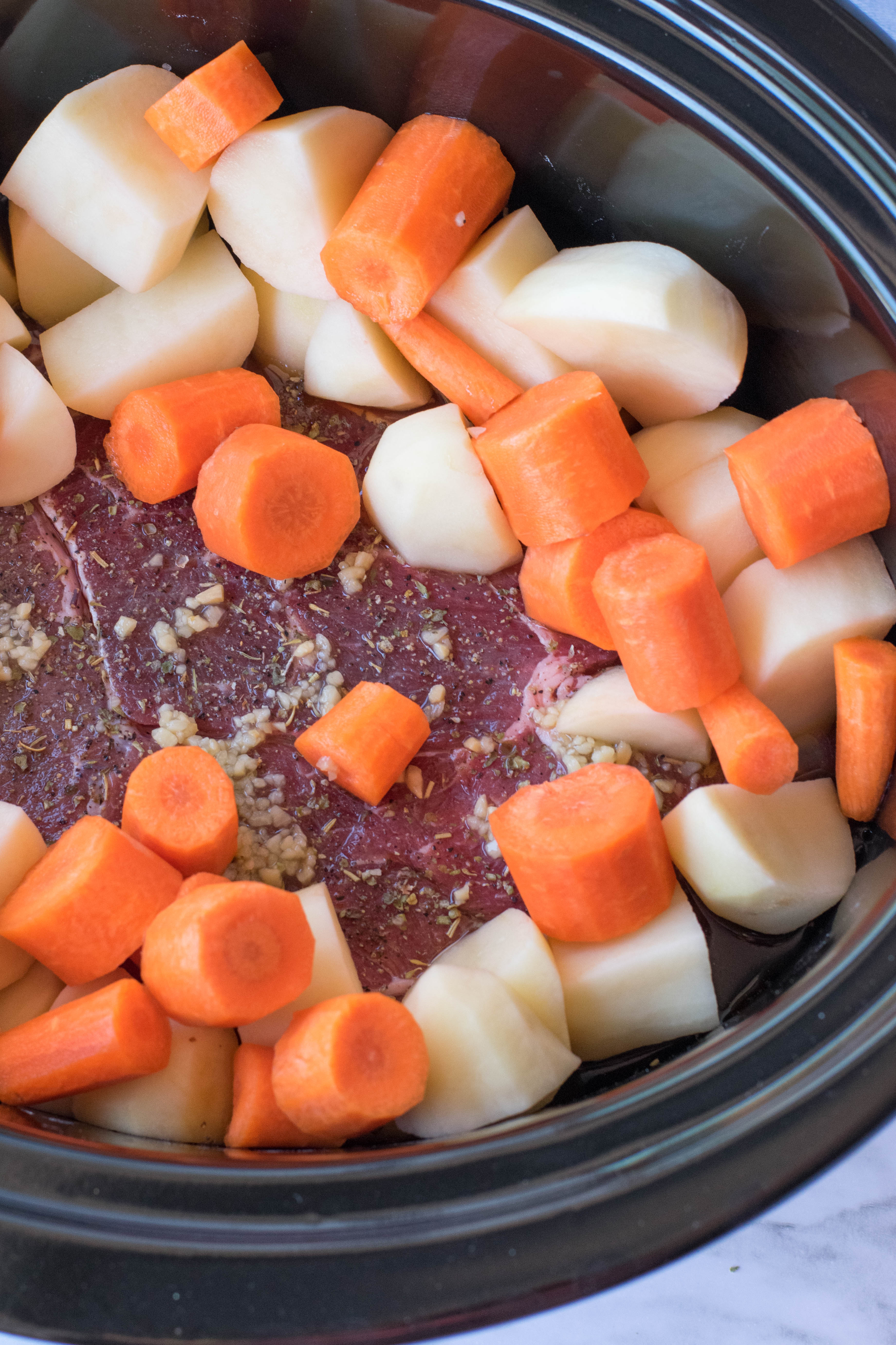 crock pot chuck roast in a black crock pot uncooked with chopped potatoes and carrots