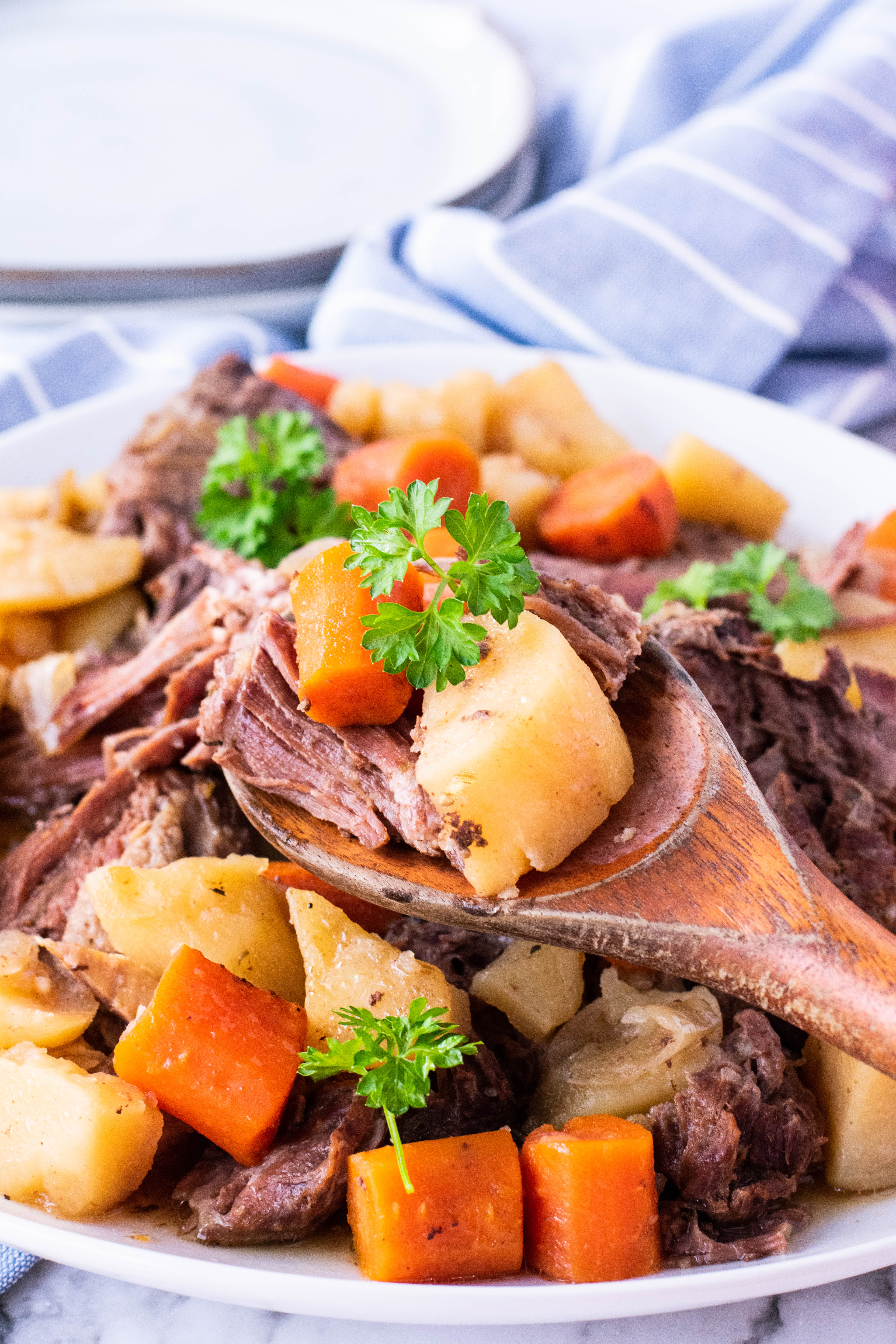 crock pot chuck roast on a plate with potatoes and carrots being lifted with a spoon