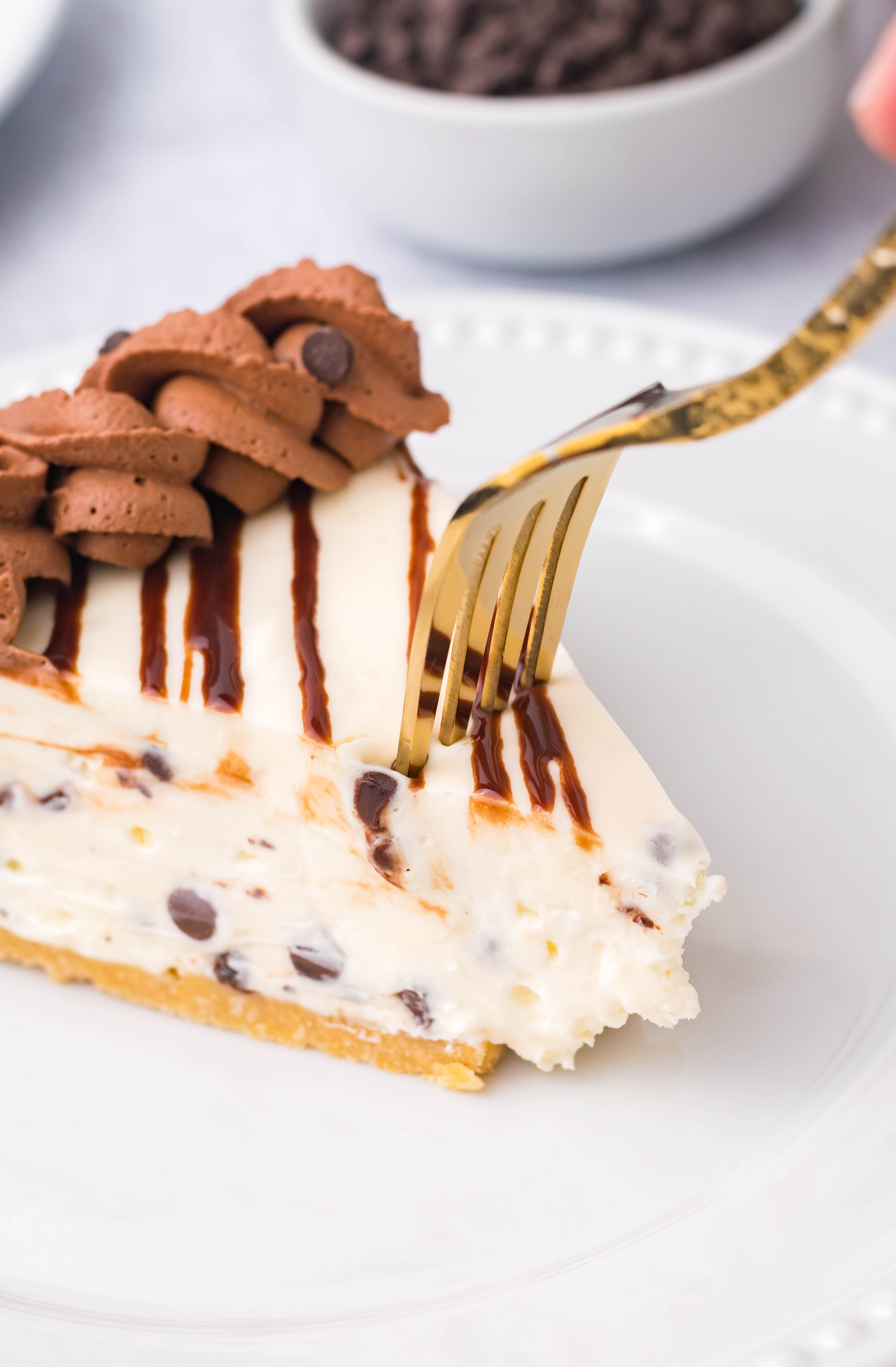 Chocolate Chip Cheesecake on a white plate with a gold fork cutting into the piece