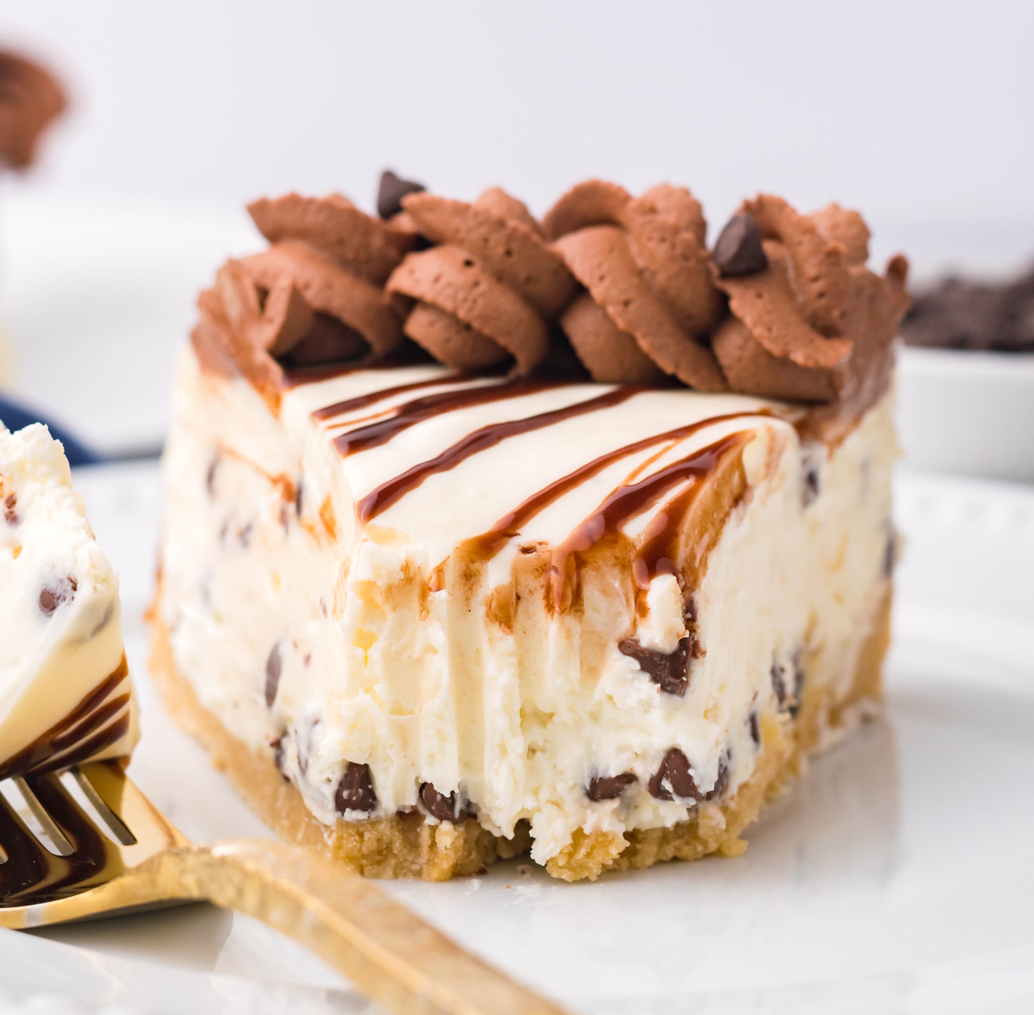 Chocolate Chip Cheesecake on a white plate with a bite taken out with a gold fork on the plate