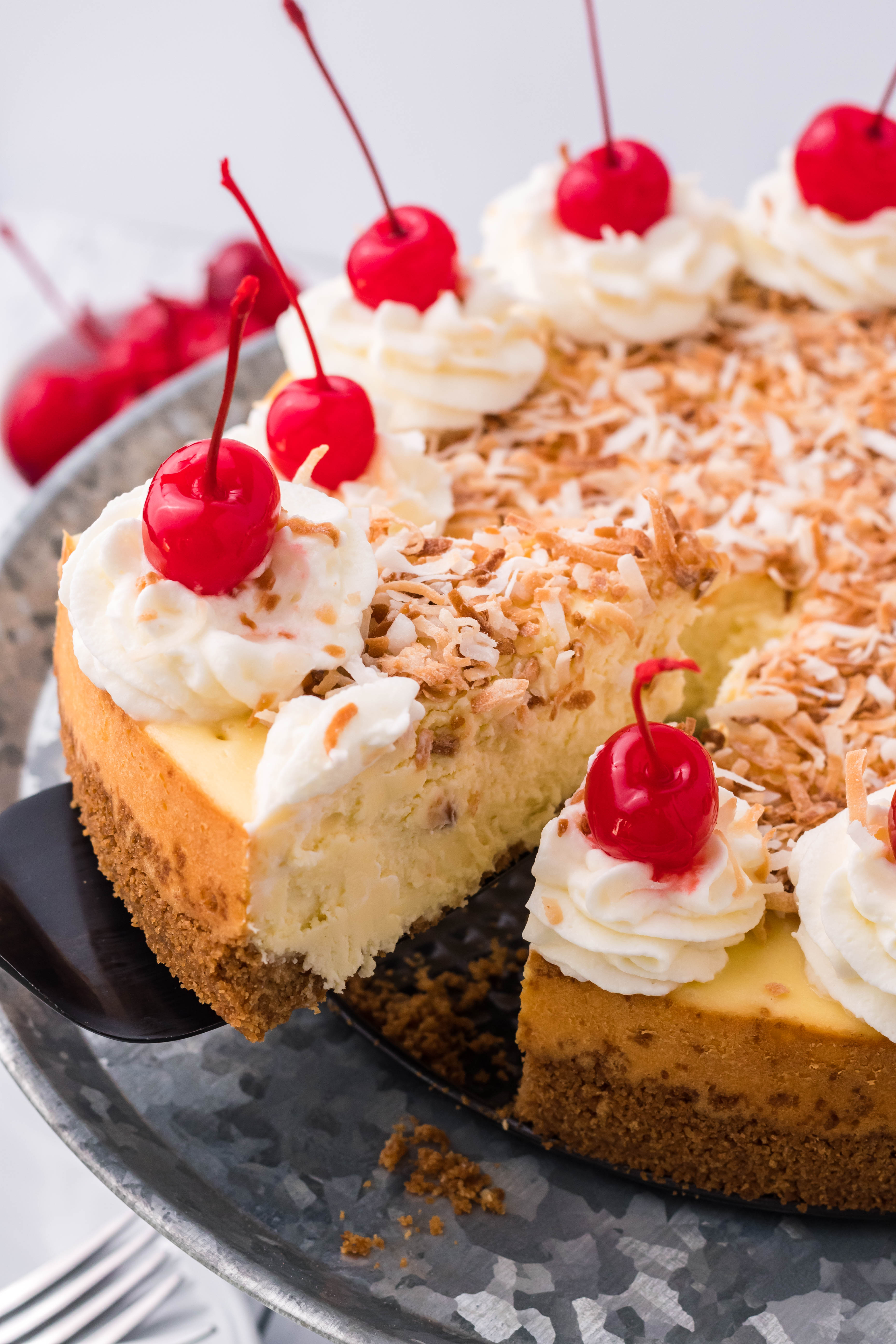 Coconut Cheesecake on a silver cake dish being lifting by a black spatula