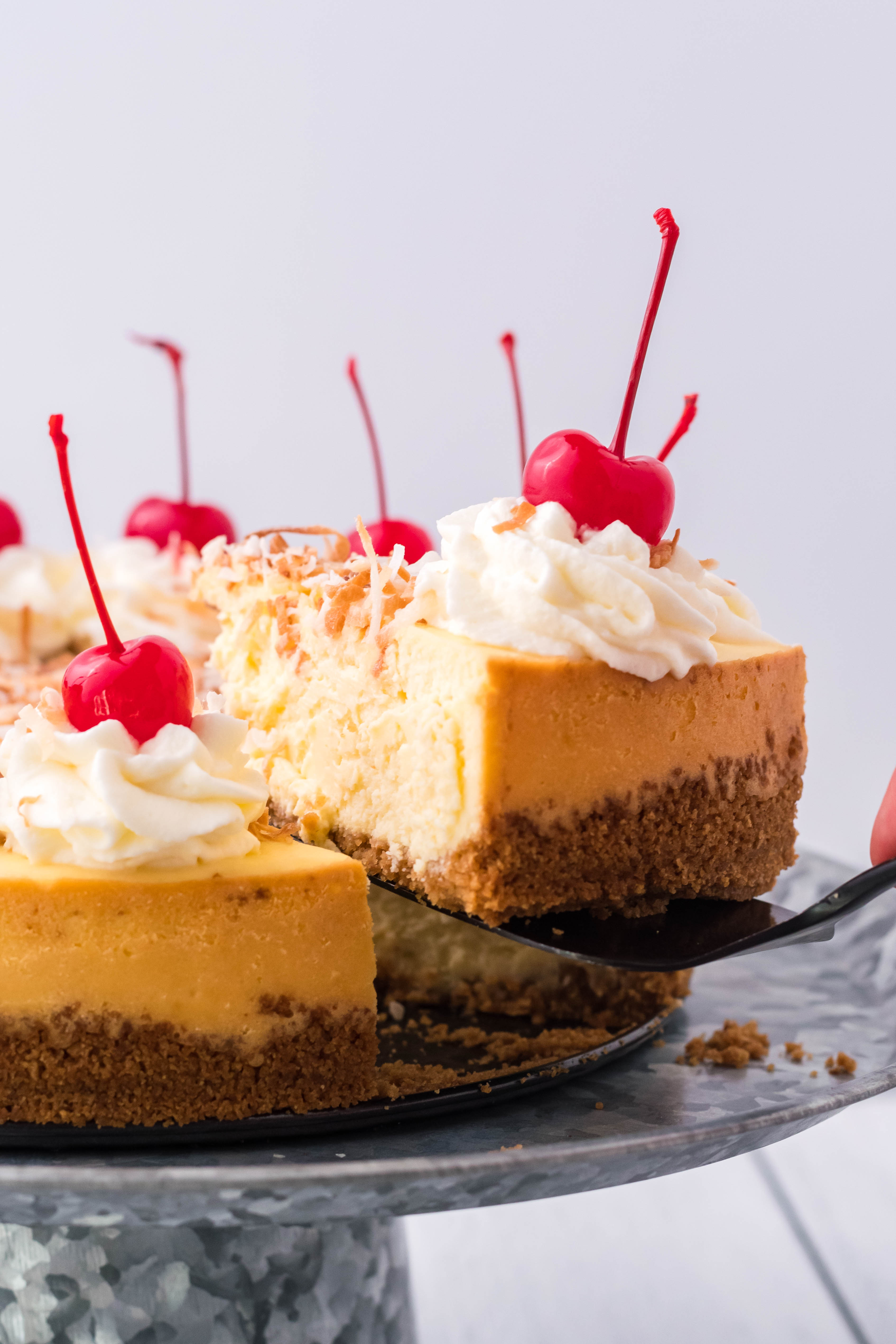 Coconut Cheesecake on a silver cake dish being lifting by a black spatula