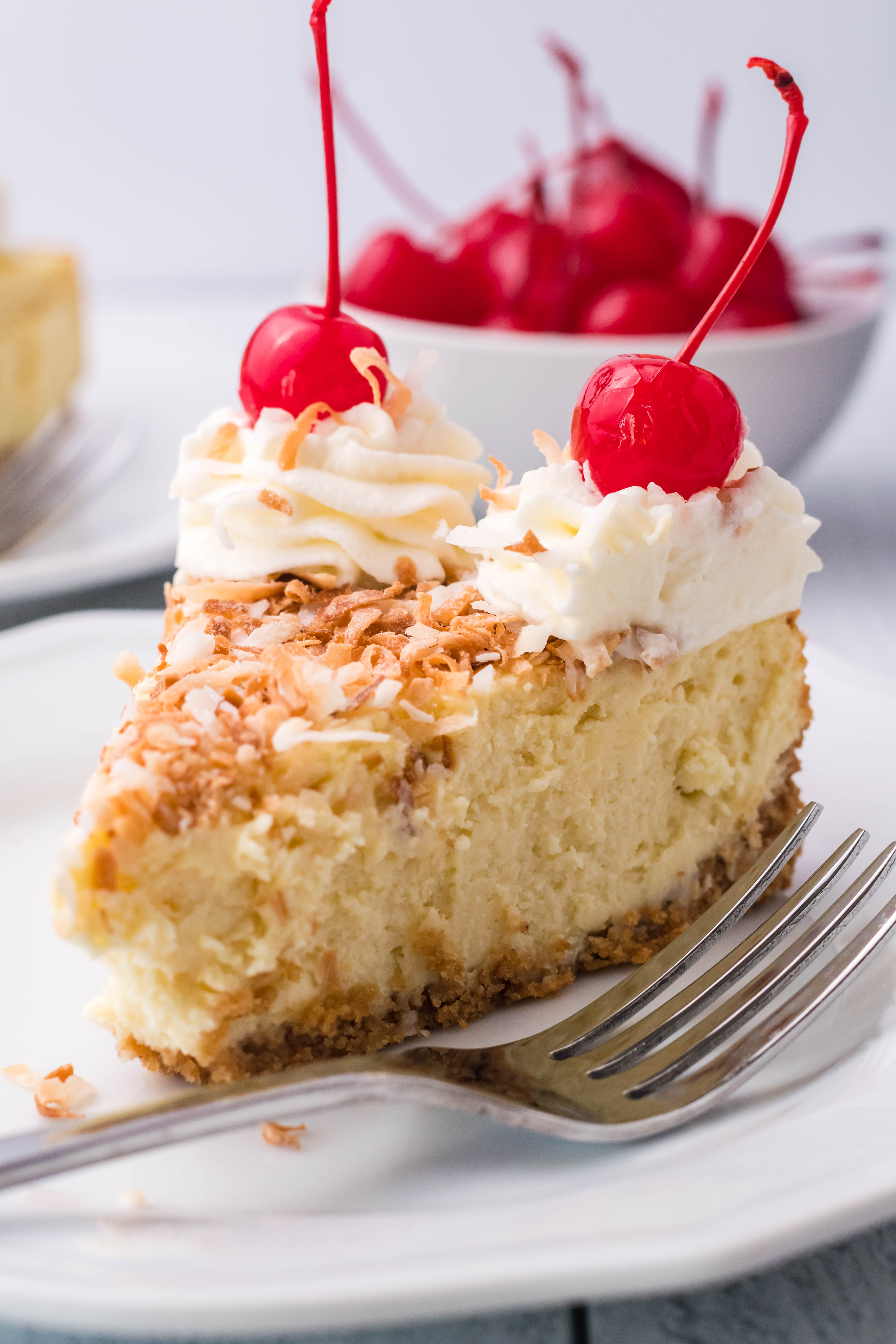 Coconut Cheesecake on a white plate topped with cherries and whipped cream