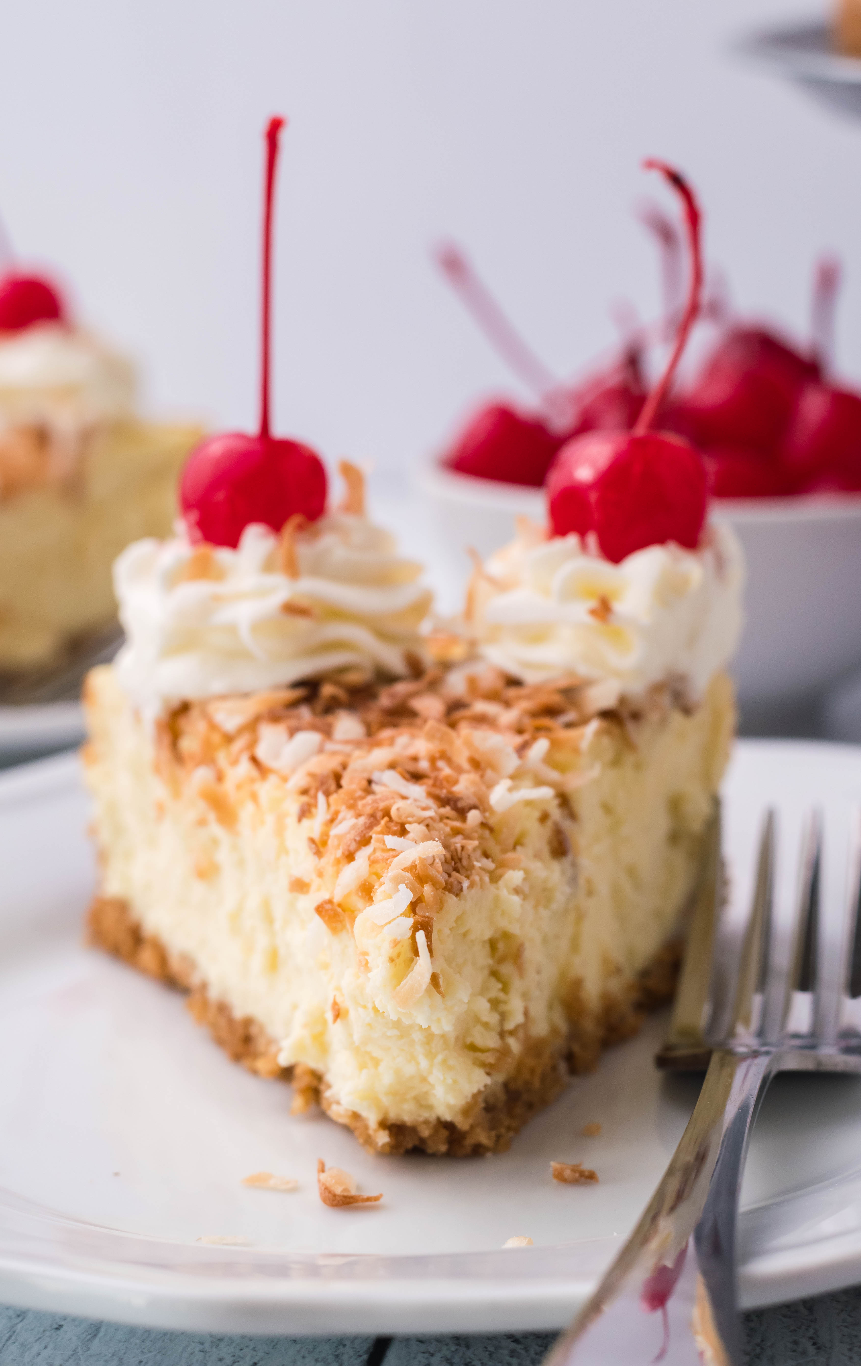Coconut Cheesecake on a white plate topped with cherries and whipped cream