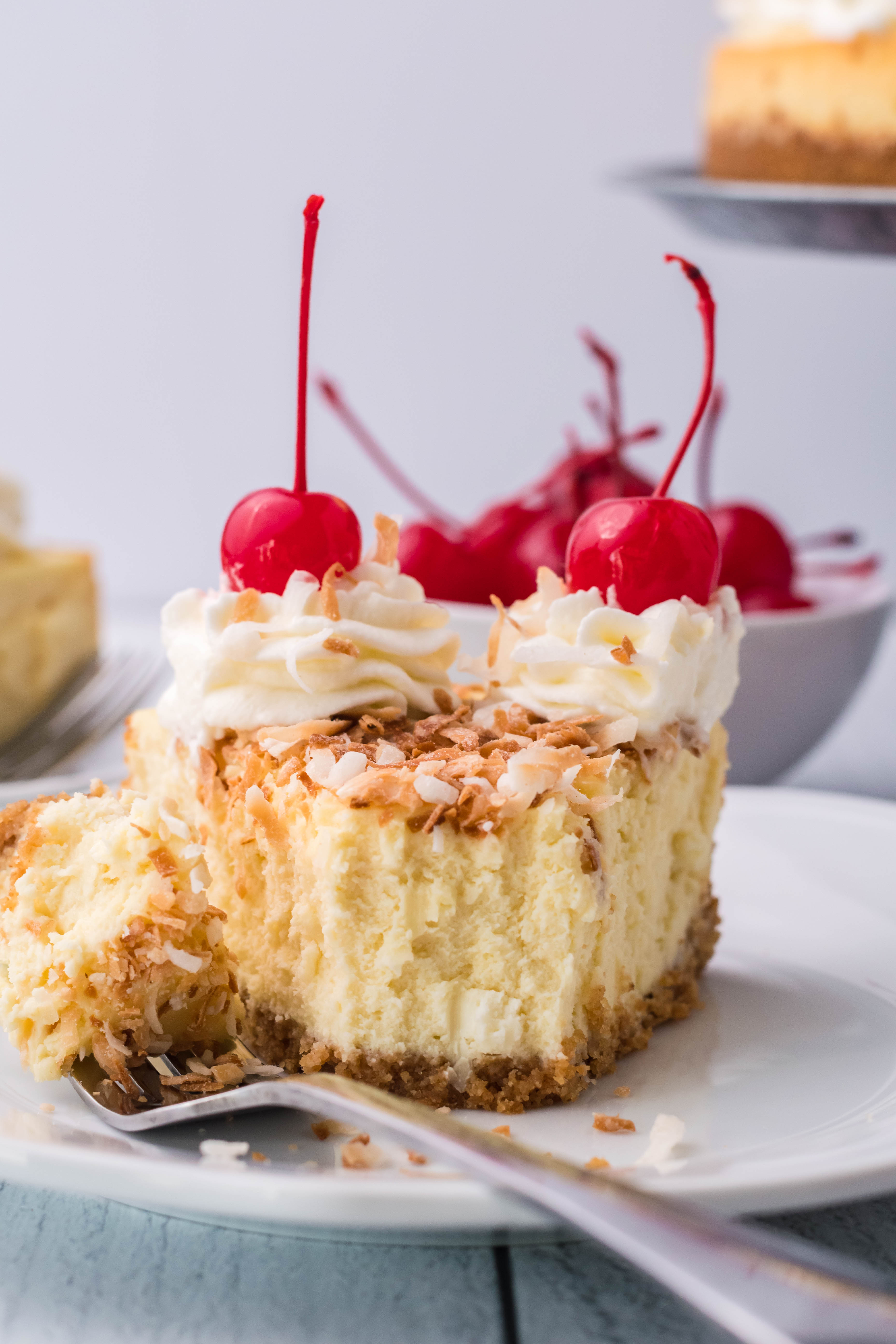 Coconut Cheesecake on a white plate topped with cherries and whipped cream
