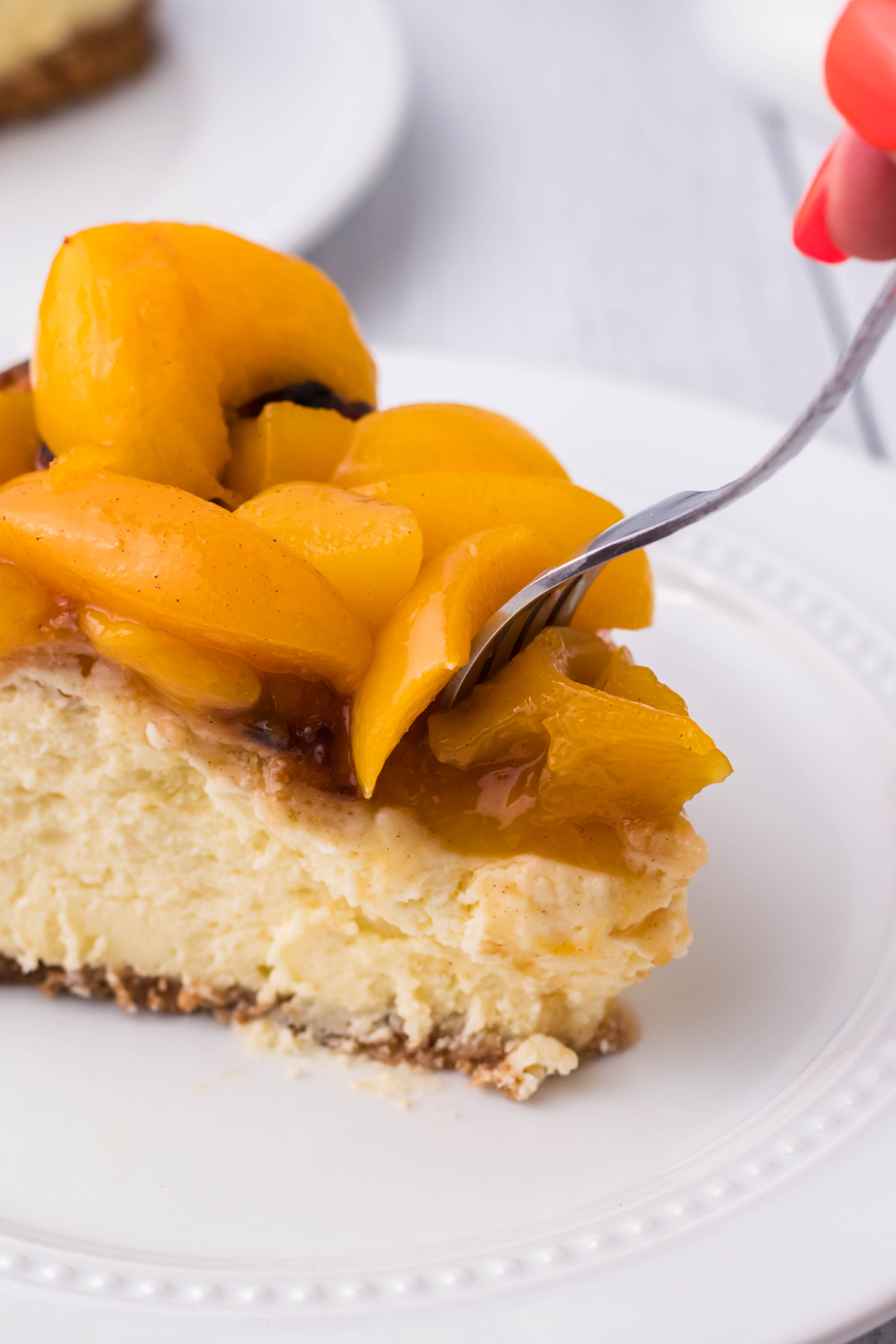 Peach Cobbler Cheesecake on a white plate with a fork slicing into it