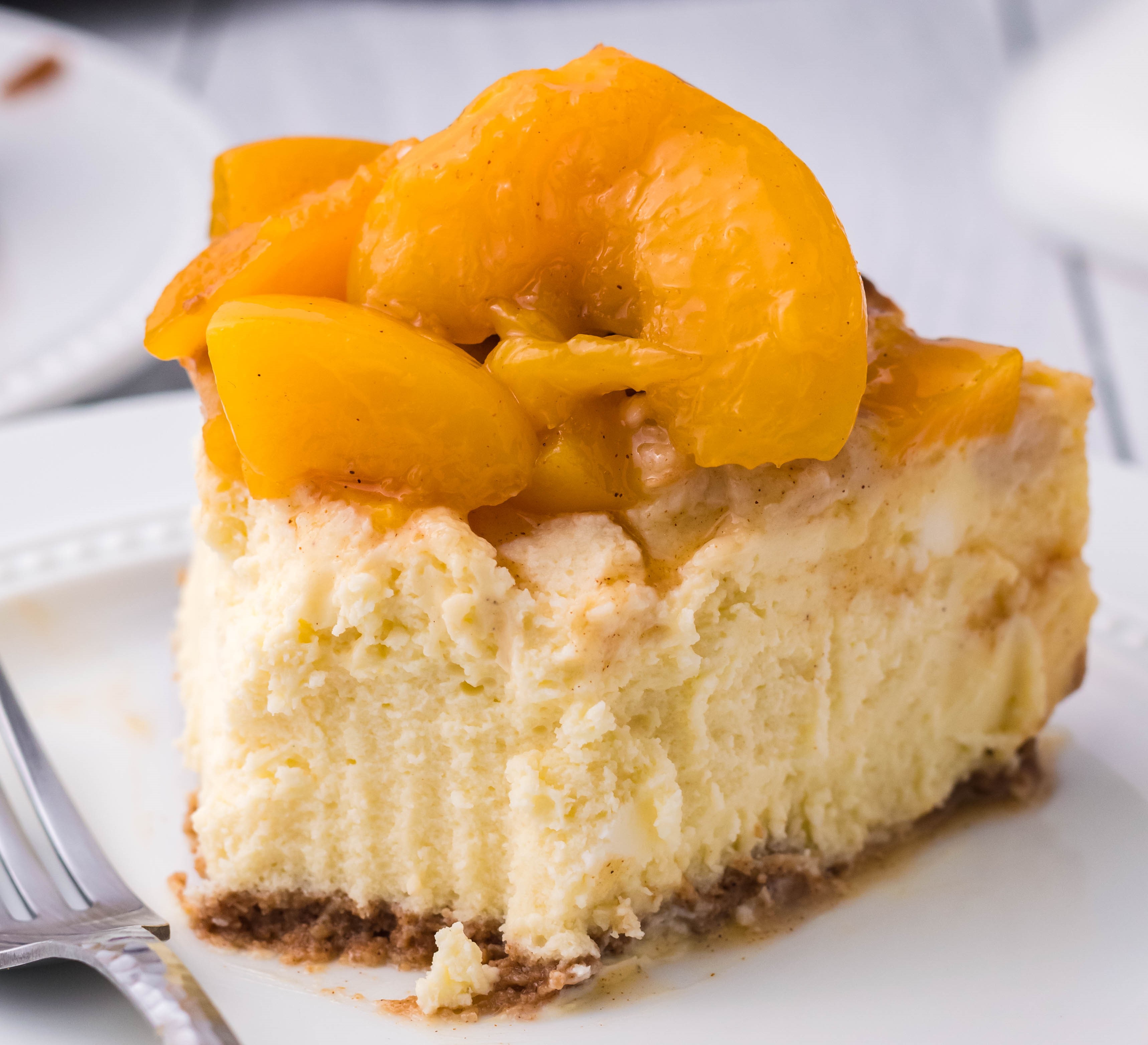 Peach Cobbler Cheesecake on a white plate with a bite taken out of the slice