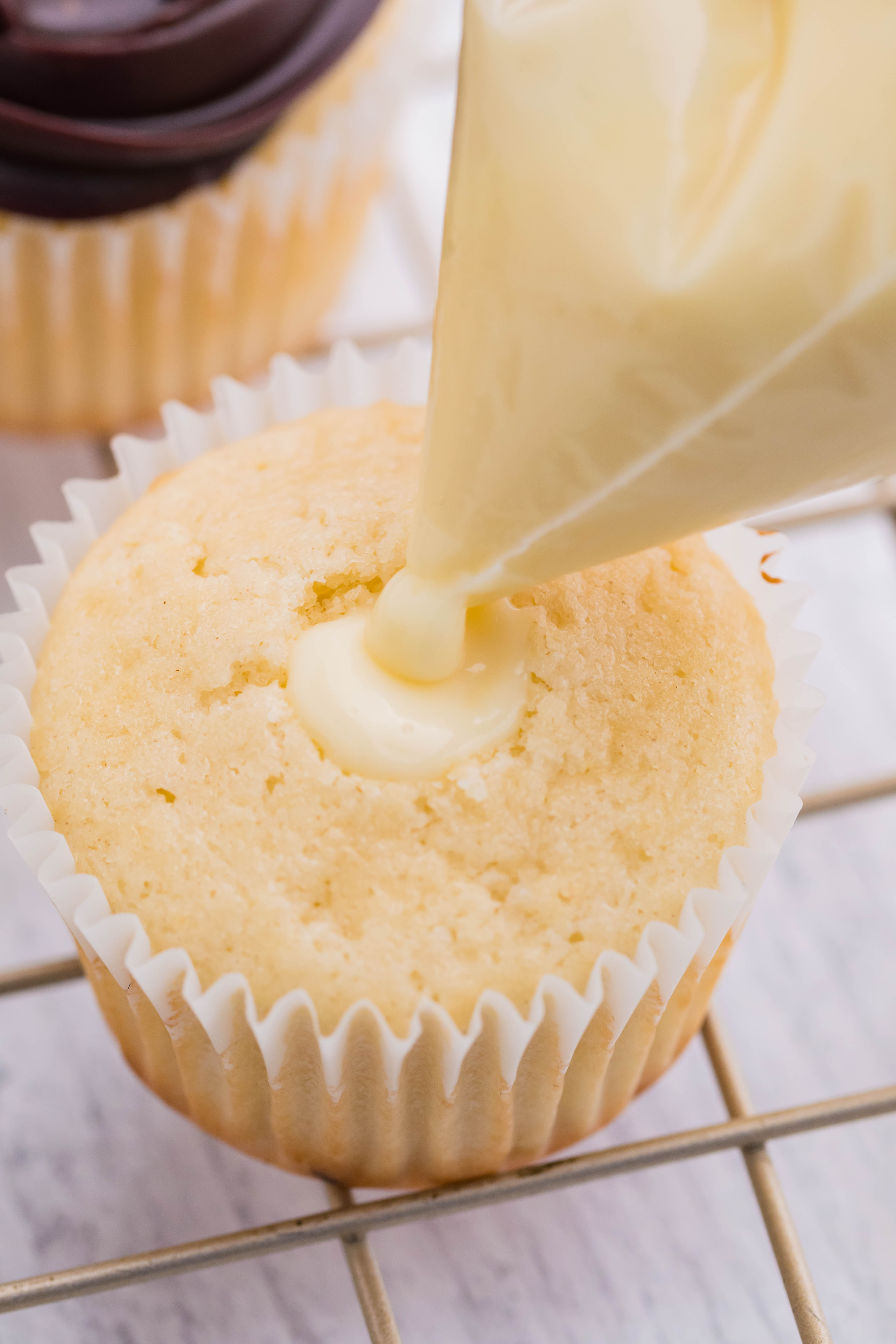 Piping the cream filling into the center of the boston cream cupcake