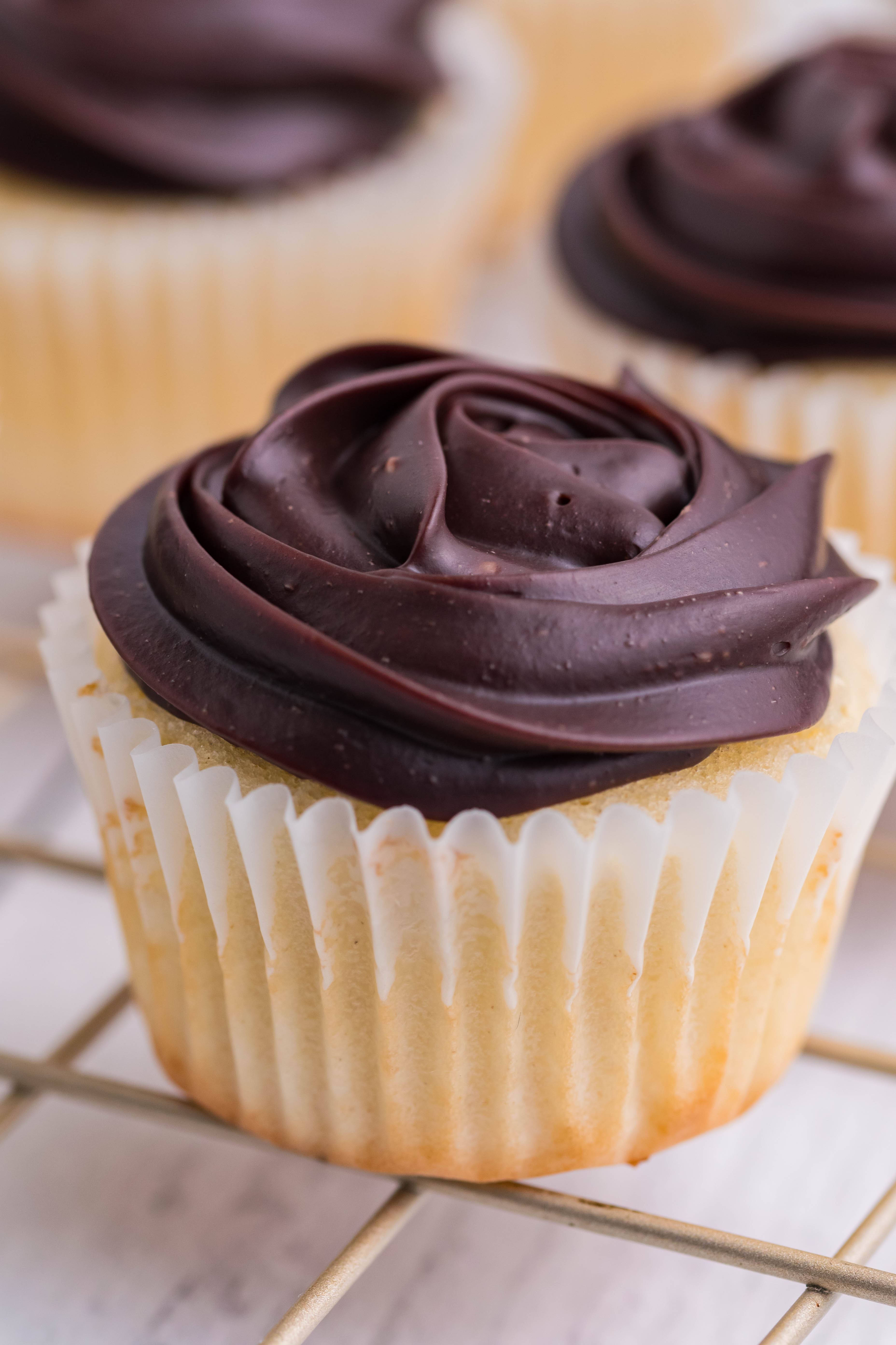 side shot of Boston Cream Cupcakes on a cooling metal rack