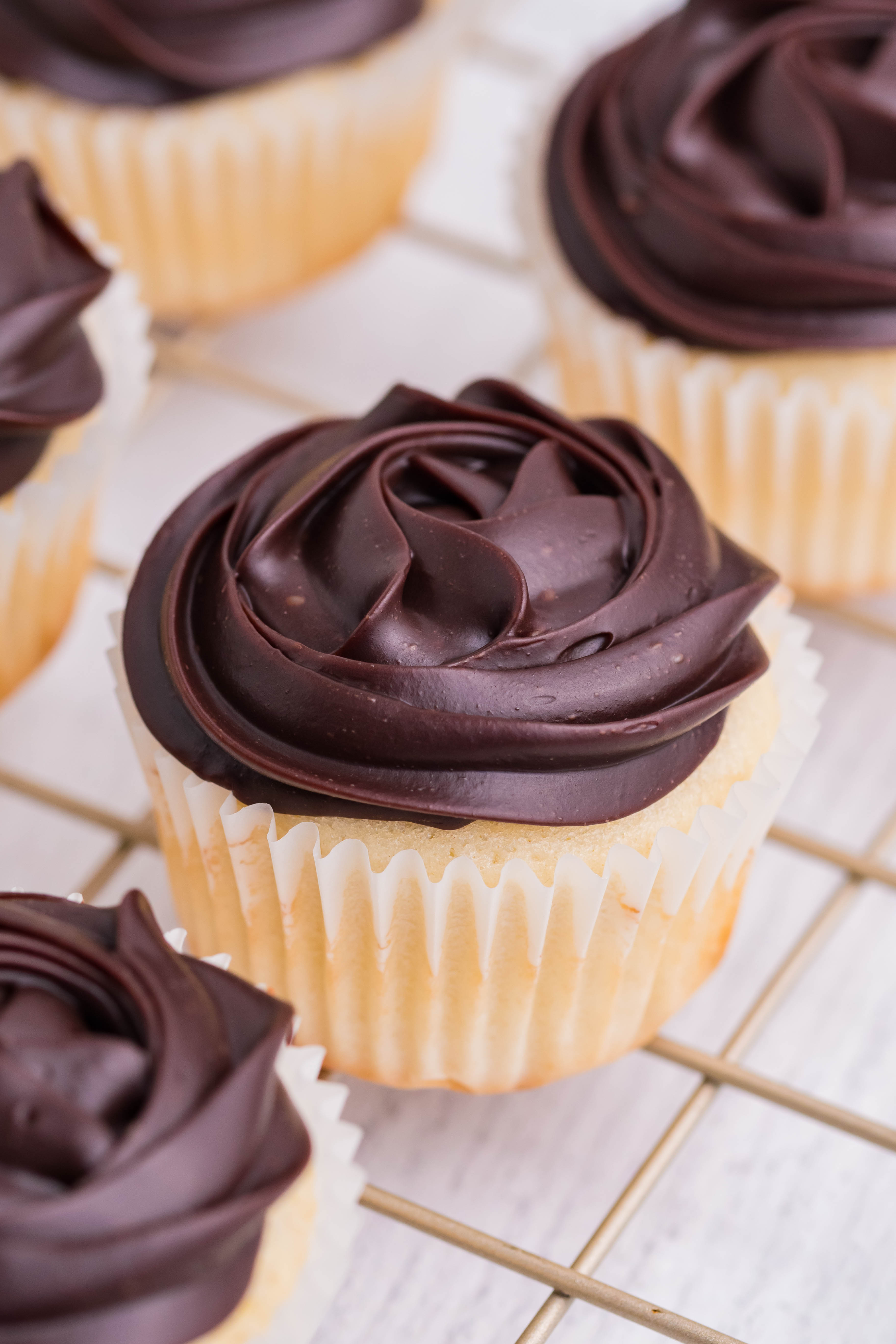 side shot of Boston Cream Cupcakes on a cooling metal rack