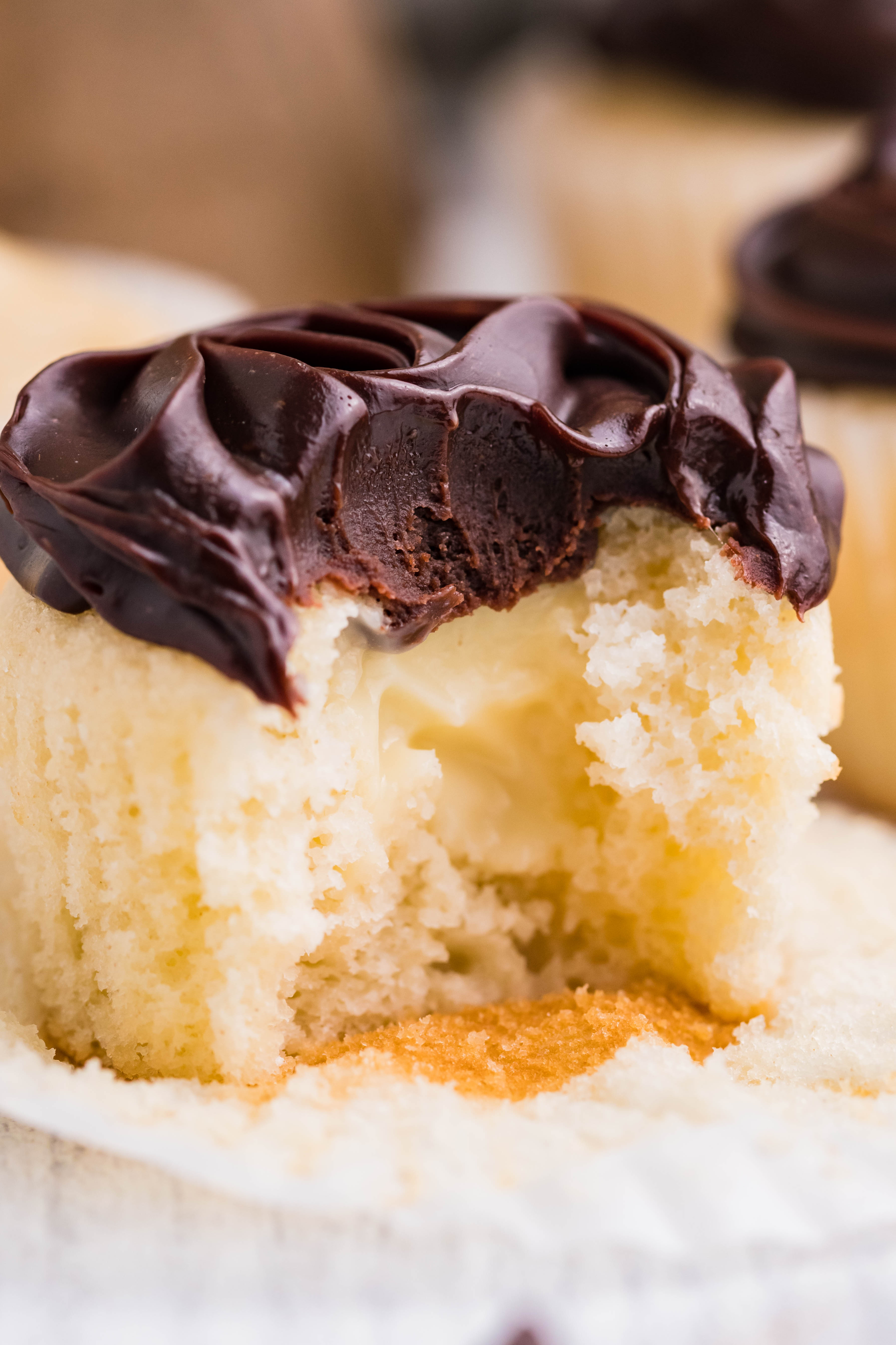 side shot of Boston Cream Cupcakes on a white counter with a bite taken out of the cupcake
