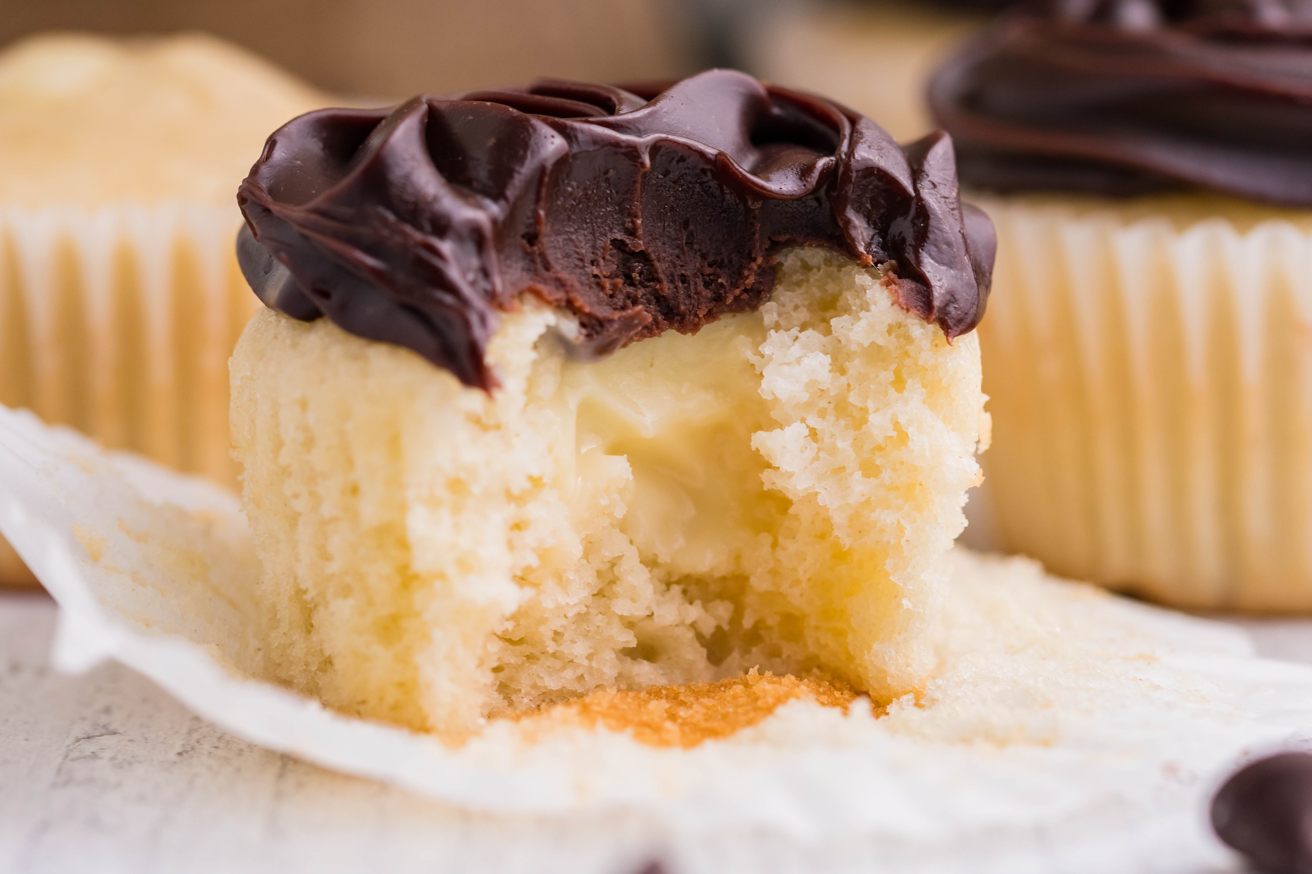 side shot of Boston Cream Cupcakes on a white counter with a bite gone