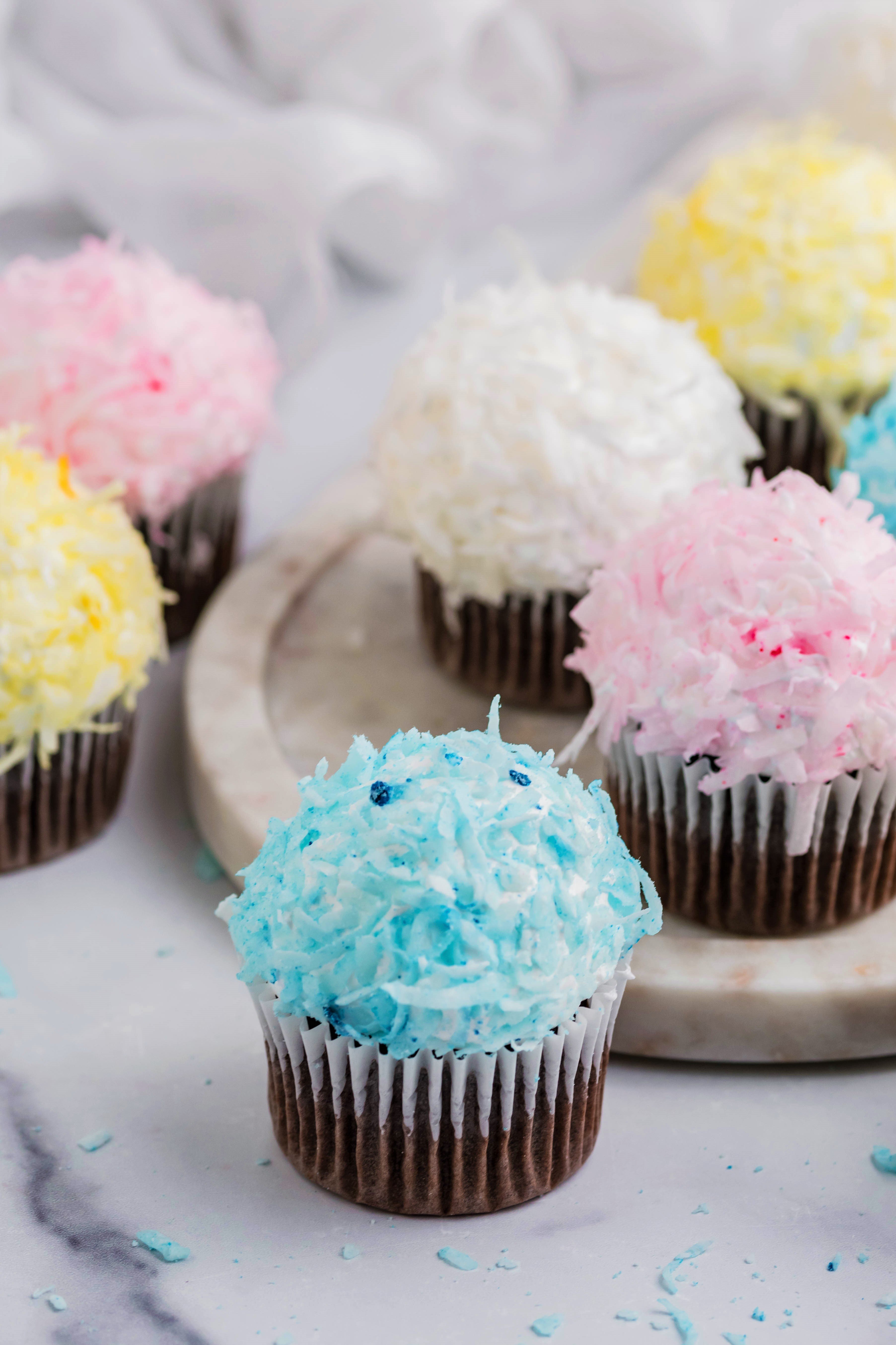 chocolate cupcakes that are Pink, yellow, white and blue topped with coconut