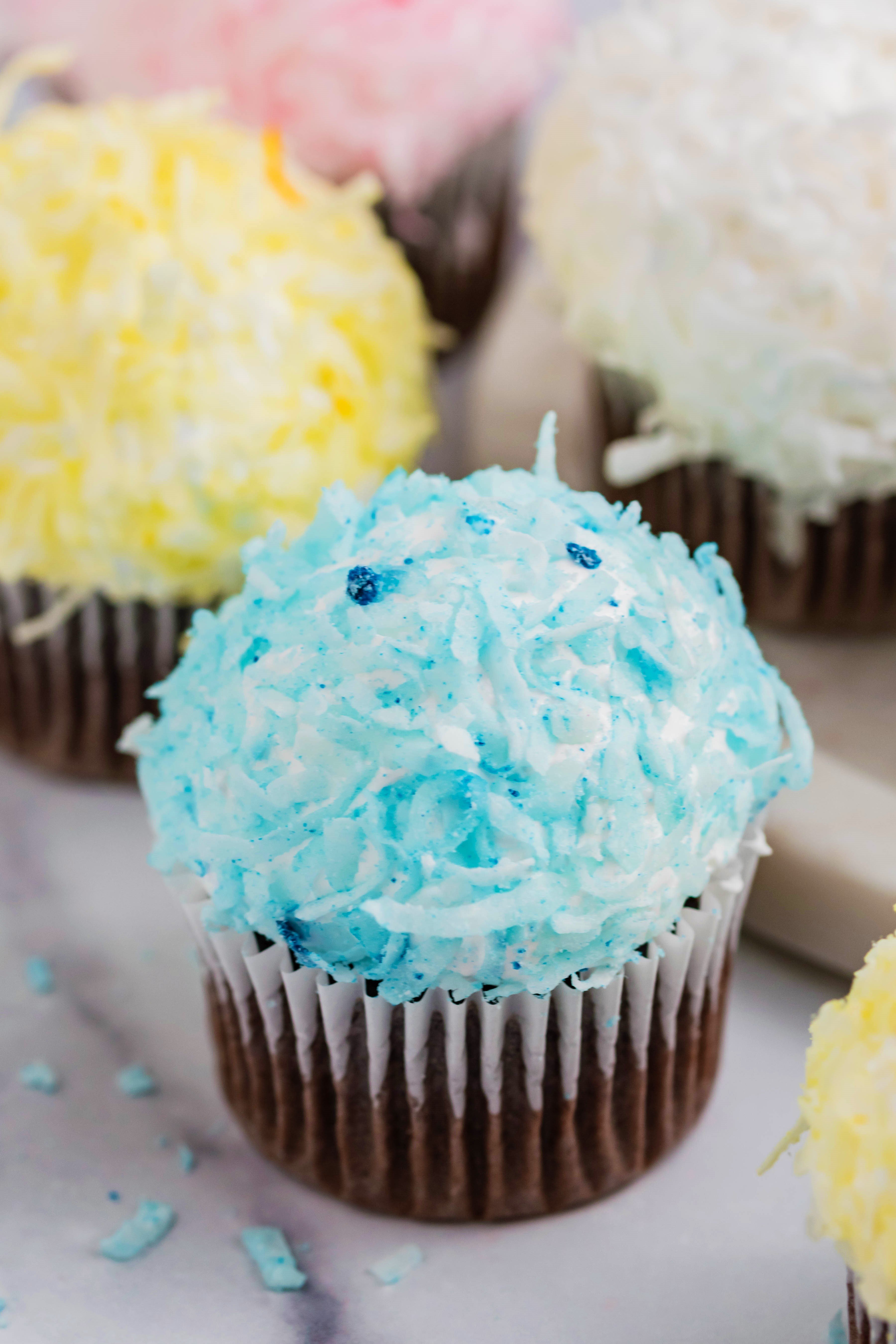 chocolate cupcakes that are Pink, yellow, white and blue topped with coconut