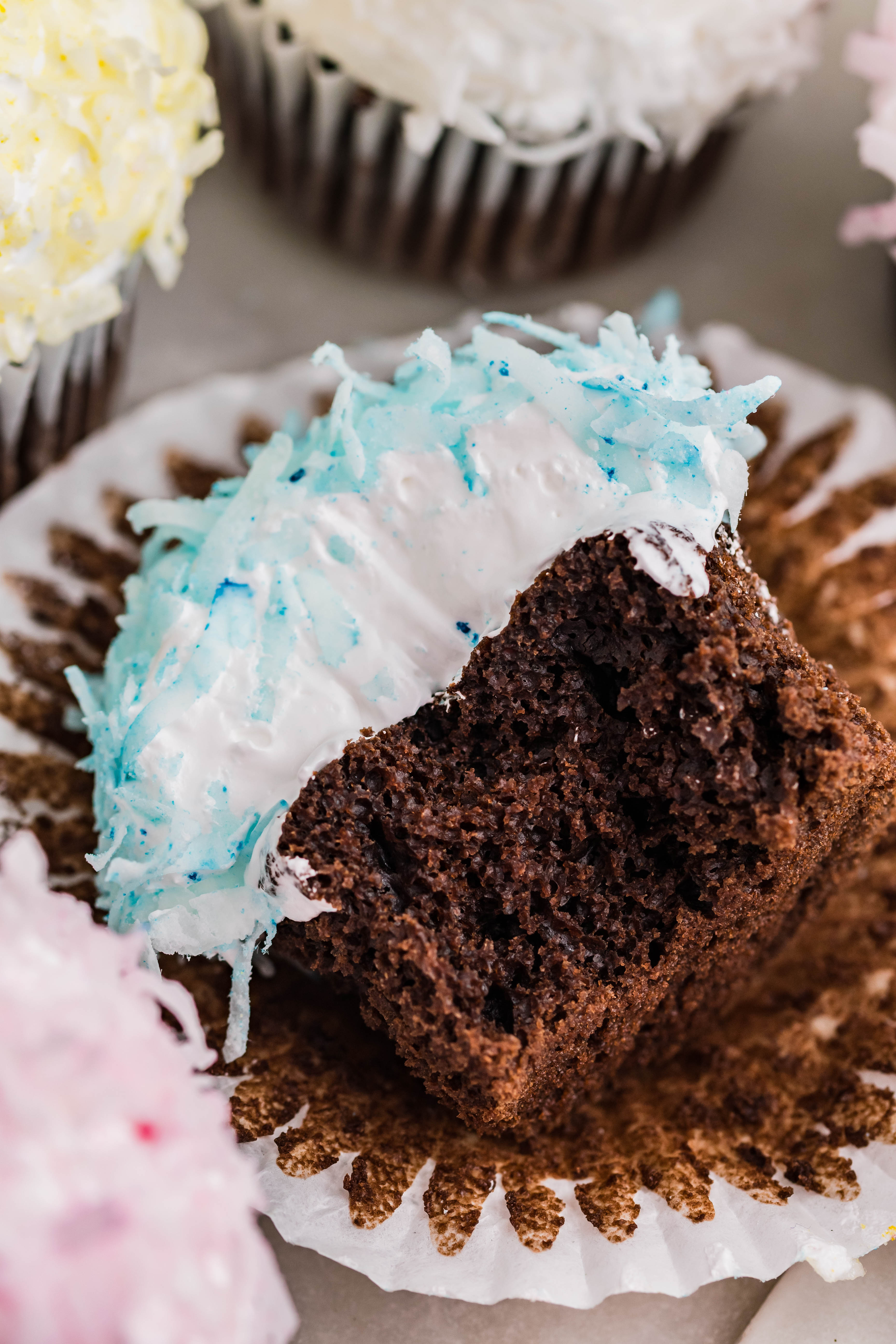 chocolate cupcake with blue coconut shavings, marshmallow frosting laying down on its side with a bite taken out of it