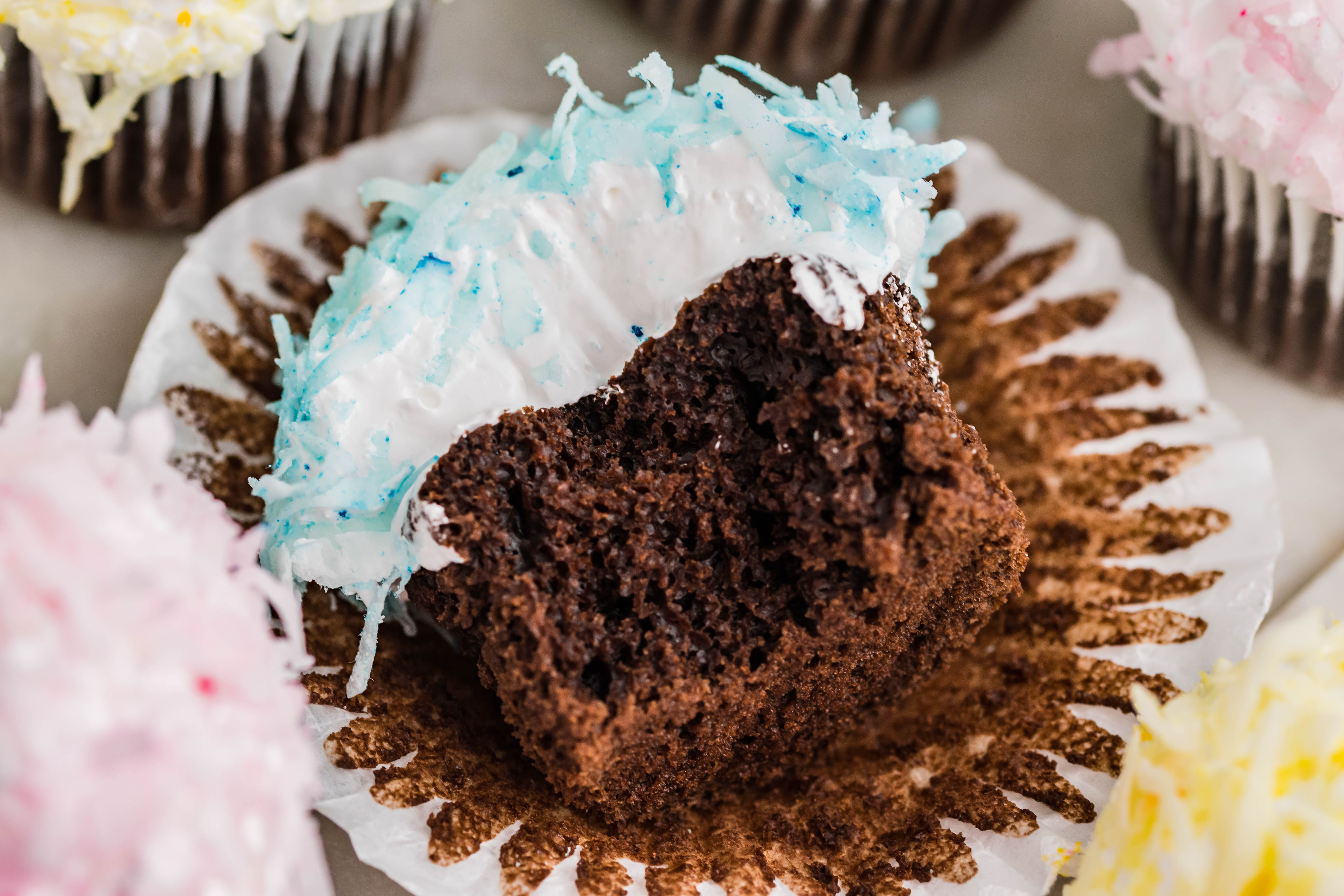 chocolate cupcake with blue coconut shavings, marshmallow frosting laying down on its side with a bite taken out of it