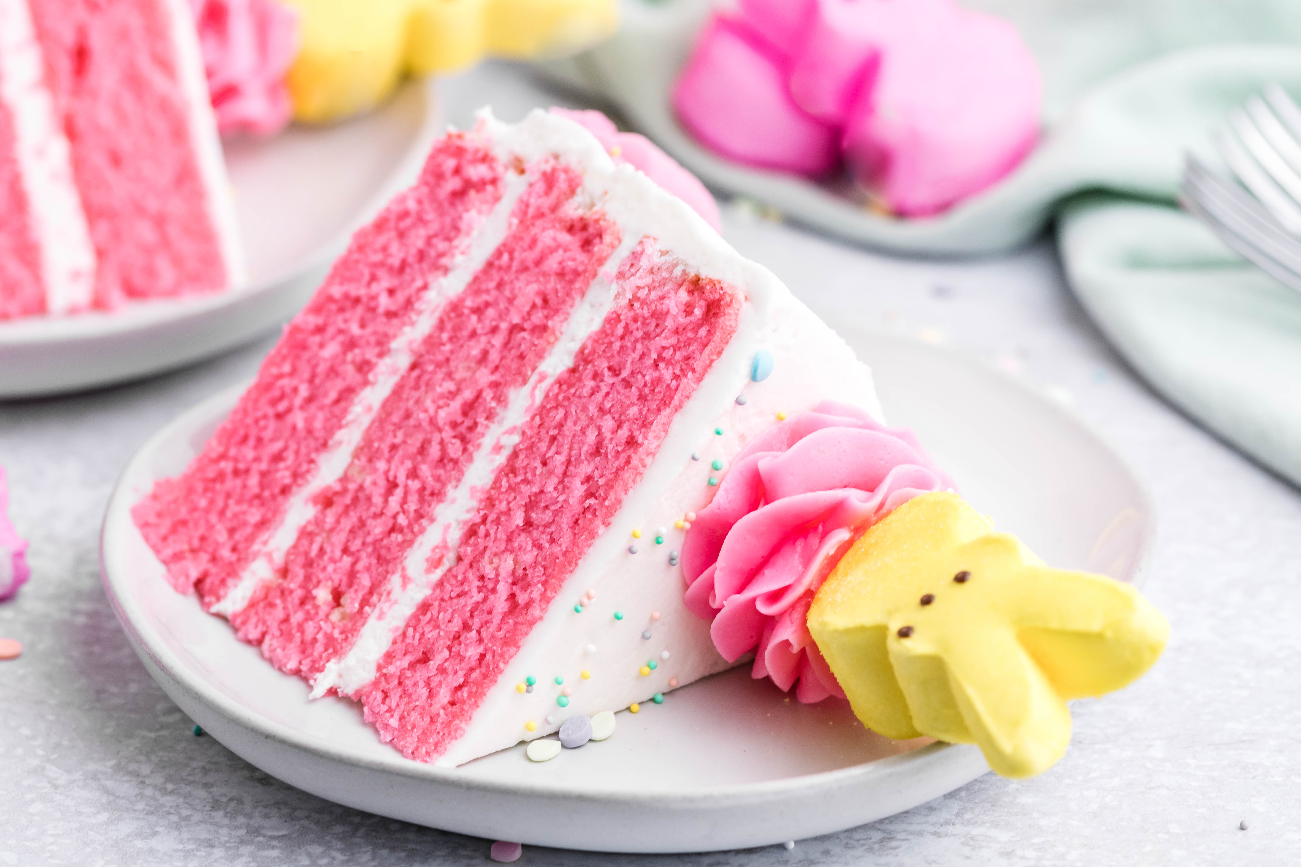 Pink Vanilla layered cake with white frosting and topped with yellow peeps for easter on a white plate