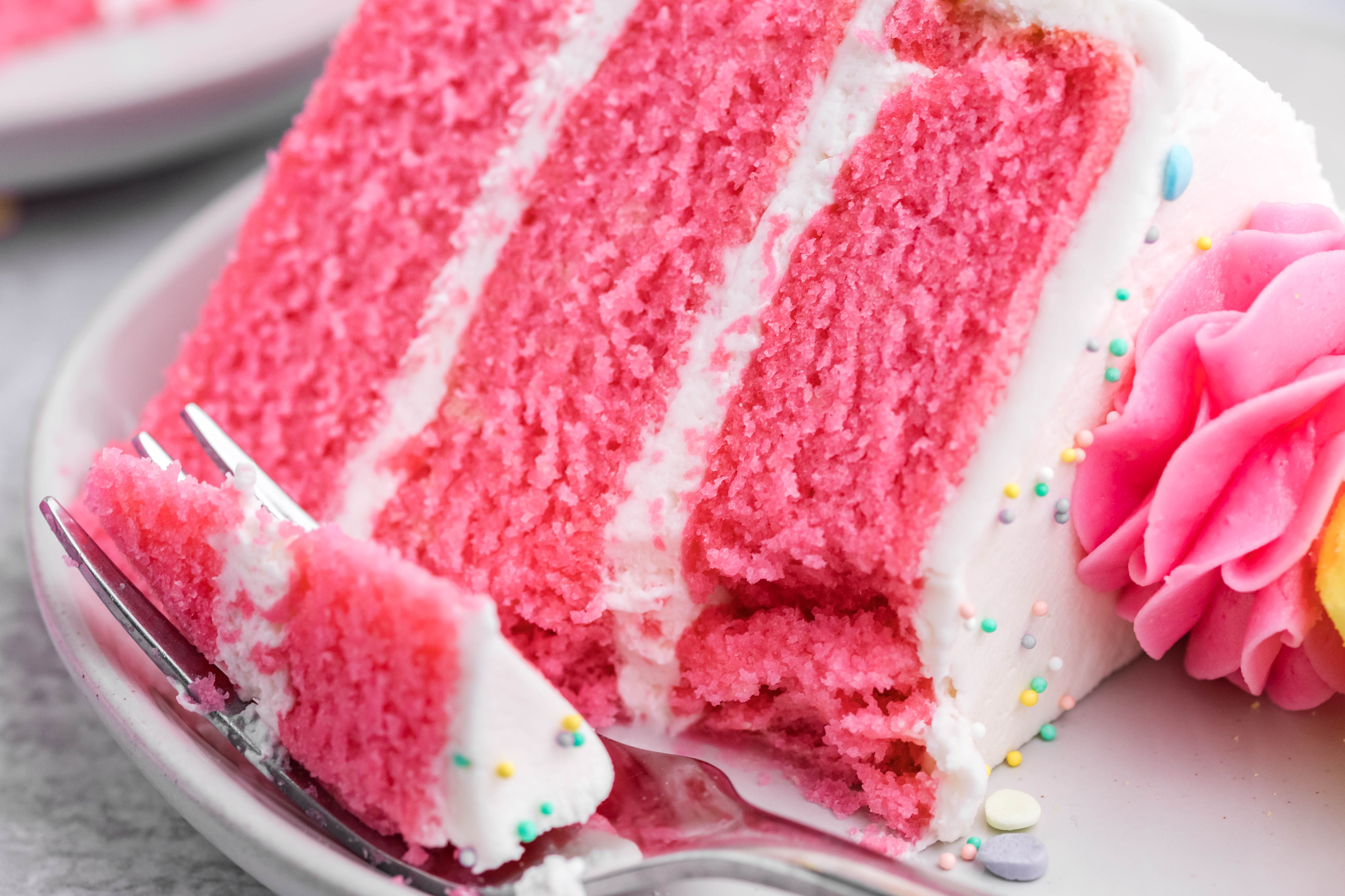 Pink Vanilla layered cake with white frosting and topped with yellow peeps for easter on a white plate with a bit gone and a bite on a fork ready to be eaten