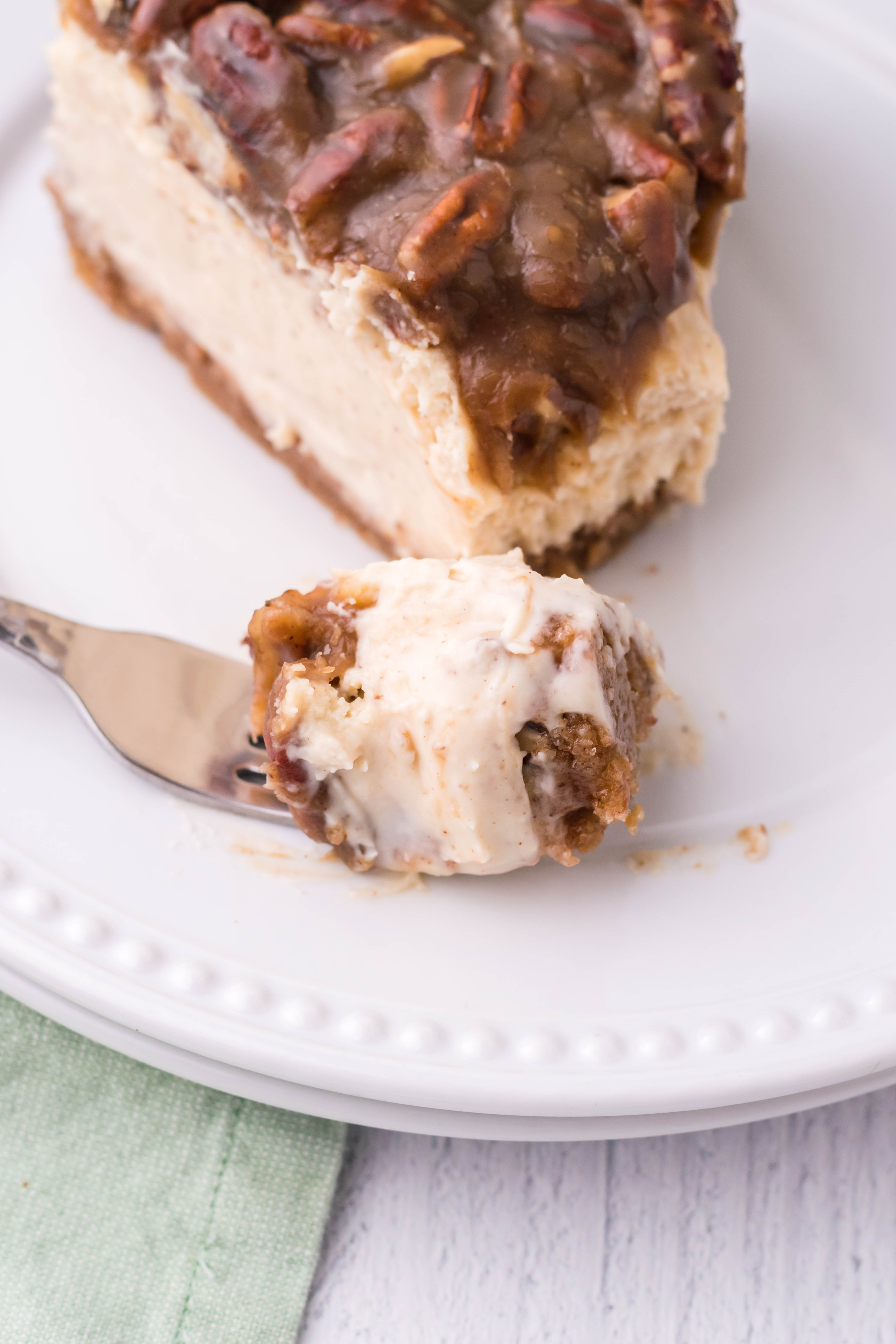 pecan pie Cheesecake slice on a white plate with a bite on a fork